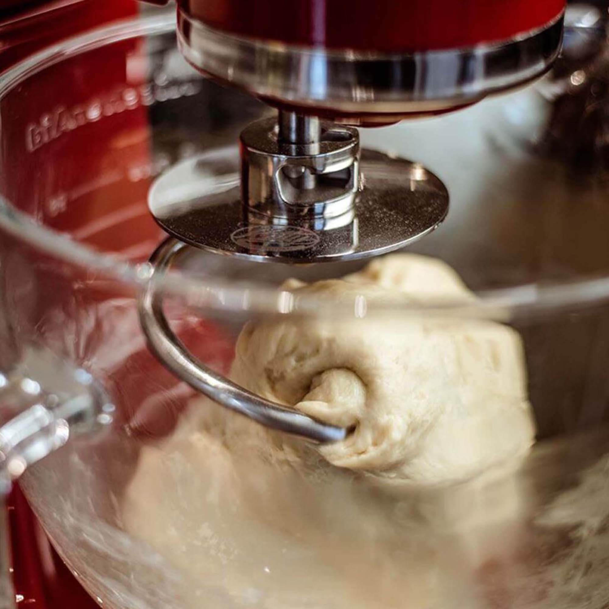 Ein Teig, der in einer Glasschüssel in einem roten Mixer gemischt wird.