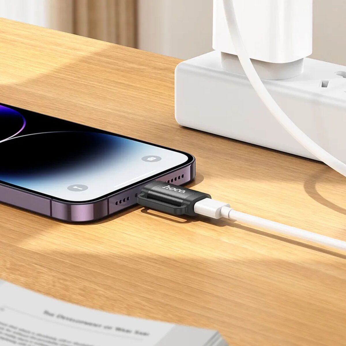 Ein Telefon wird über einen Adapter an ein Ladegerät angeschlossen, auf einer Holzoberfläche.