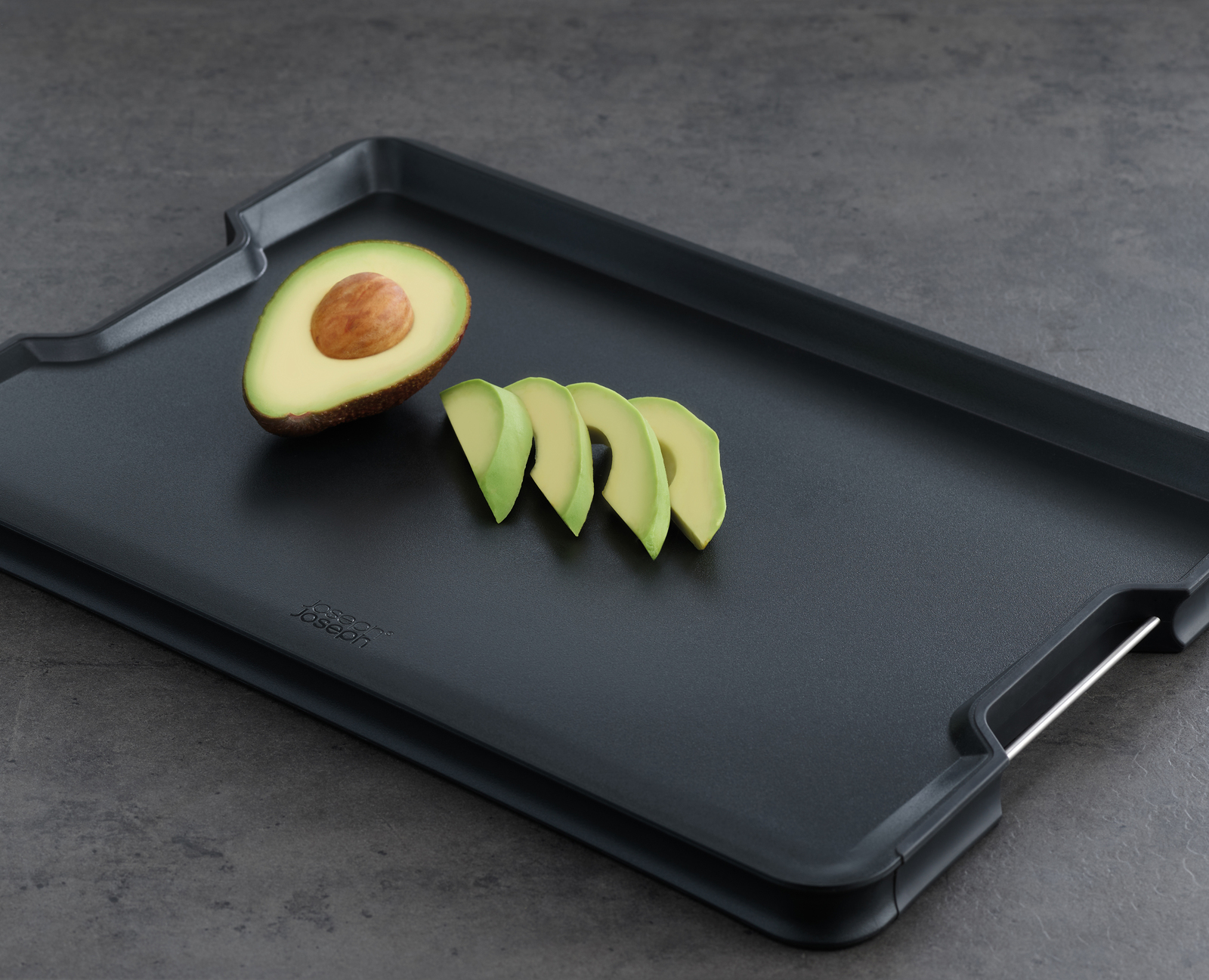 Halbe Avocado, Avocado in Scheiben auf einem schwarzen Schneidebrett. Grauer Hintergrund.