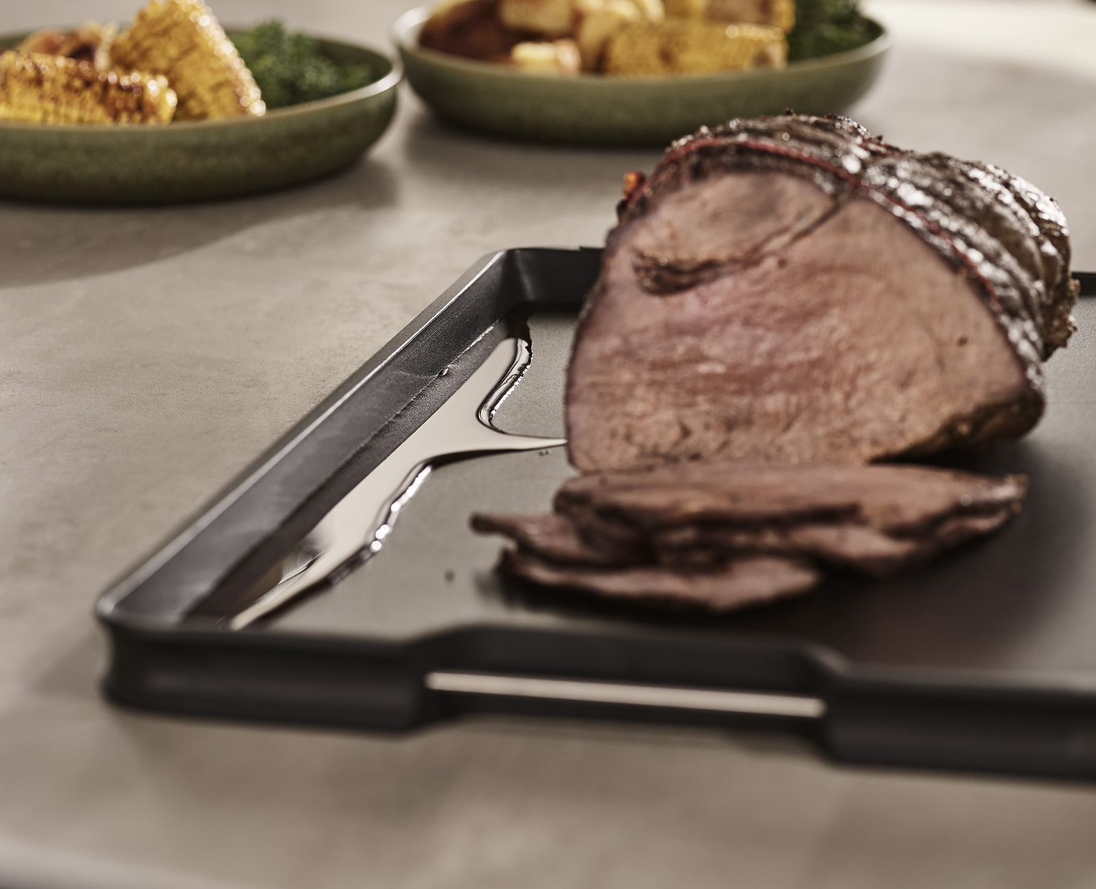 Geschnittenes Bratenfleisch auf schwarzem Tablett mit Öl. Mais und andere Gerichte im Hintergrund.