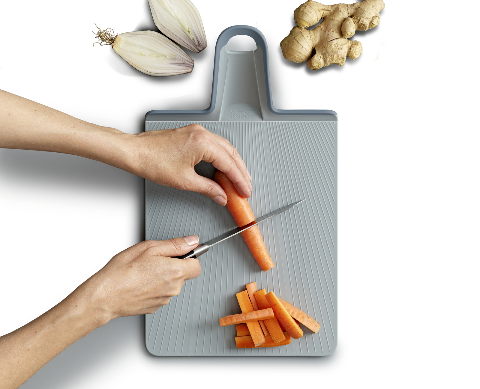 Una persona corta una zanahoria en una tabla de cortar gris. Ingredientes como jengibre y cebollas están en el fondo.