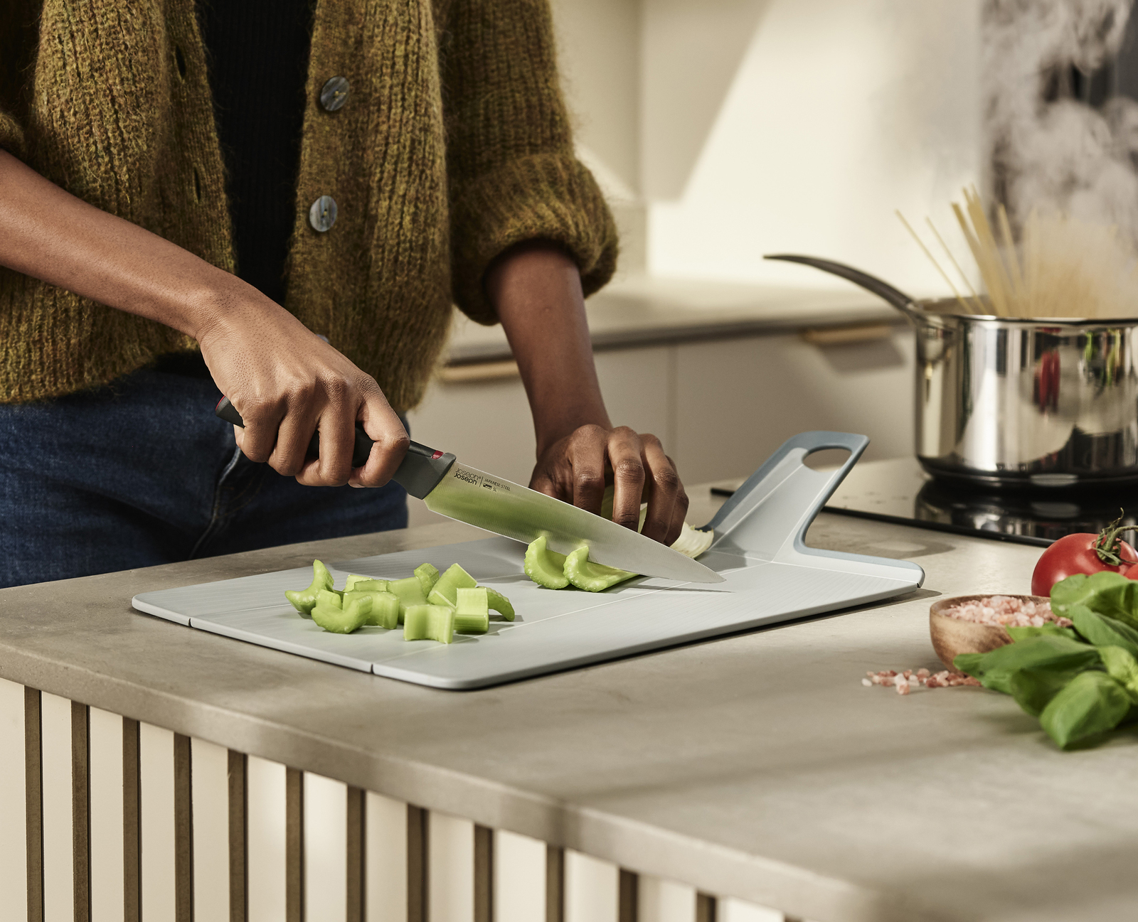 Persona cortando verduras en una tabla de cortar gris con un cuchillo.