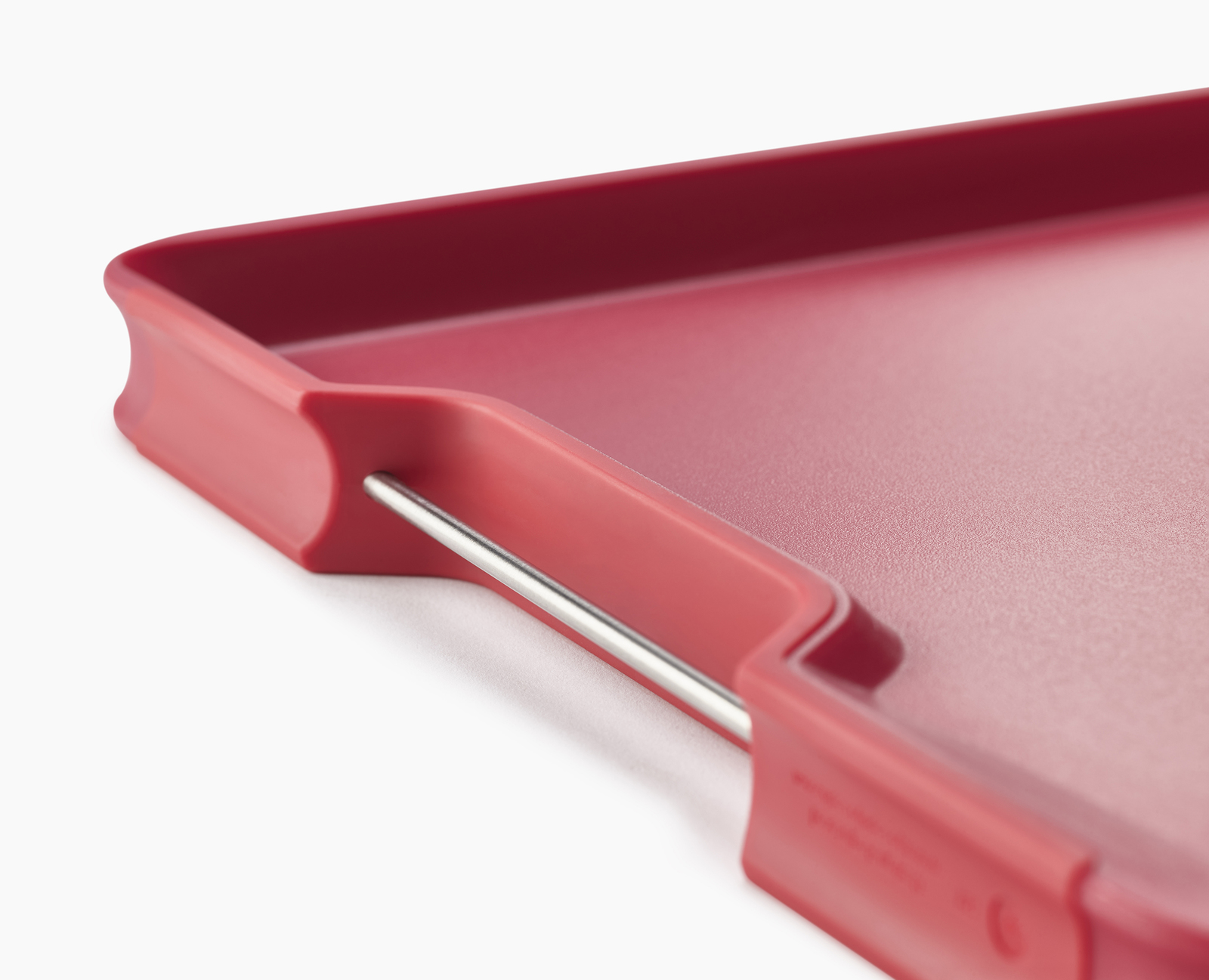 Primer plano de una tabla de cortar roja con un asa de barra metálica.