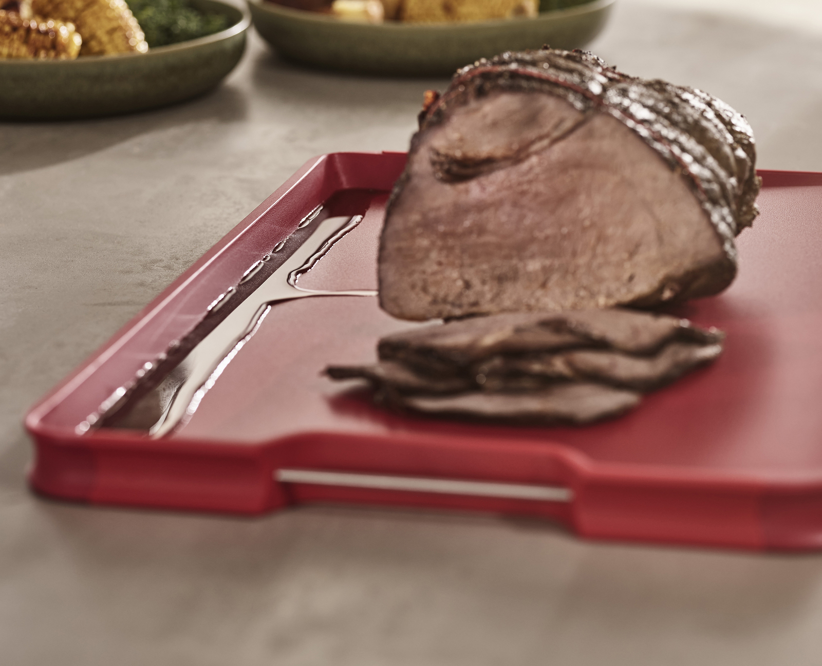 Una tabla de cortar roja con un asado y carne en rodajas. Otros cuencos son visibles en el fondo.