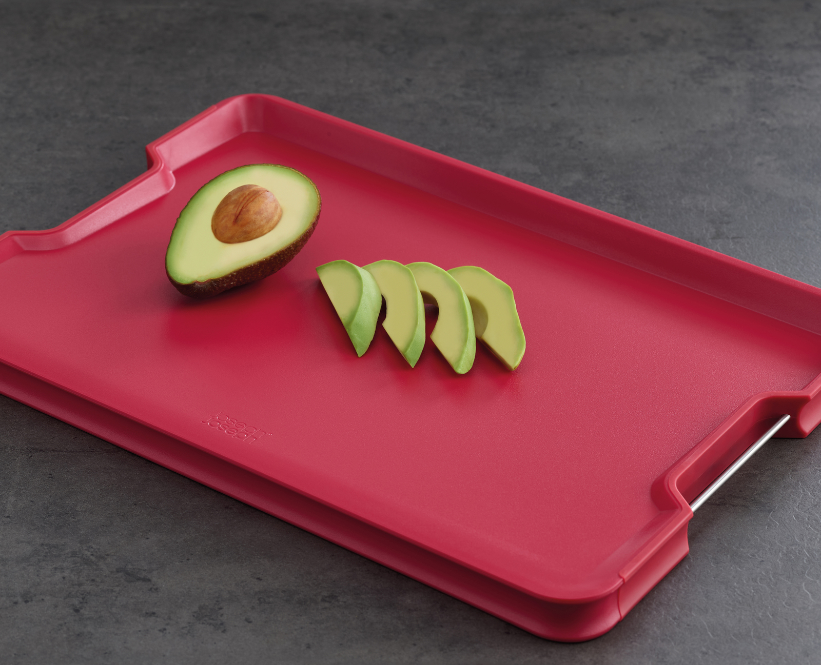 Mitades y rodajas de aguacate sobre una tabla de cortar roja.