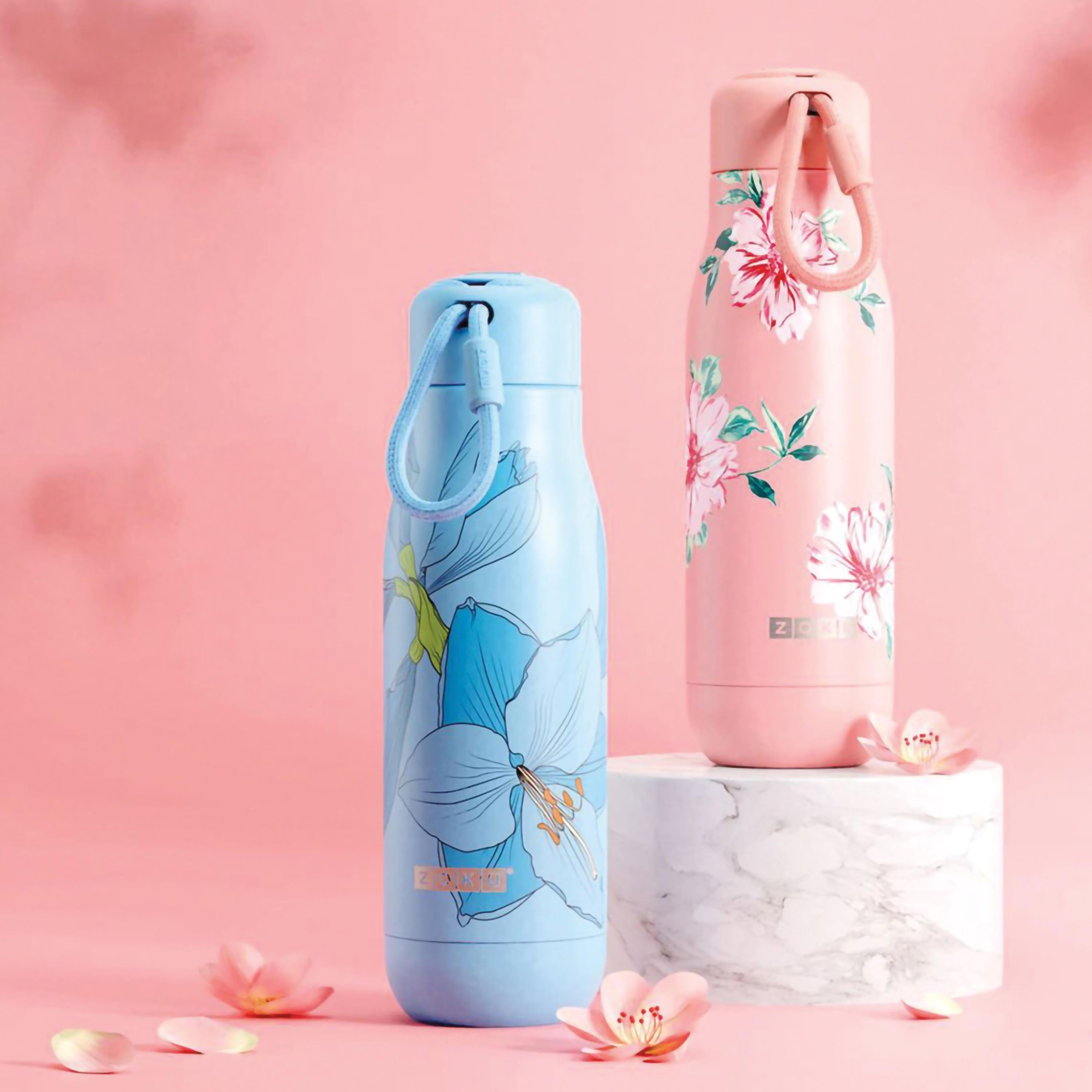 Zwei florale Wasserflaschen auf rosa Oberfläche. Eine ist blau, eine ist rosa, beide mit Griff.