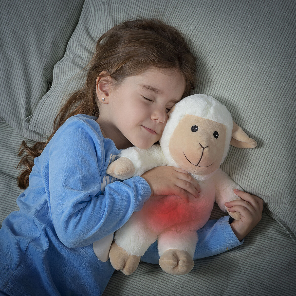Una bambina che abbraccia una pecora giocattolo. La pecora ha un'area rossa sulla pancia. La bambina sta dormendo.