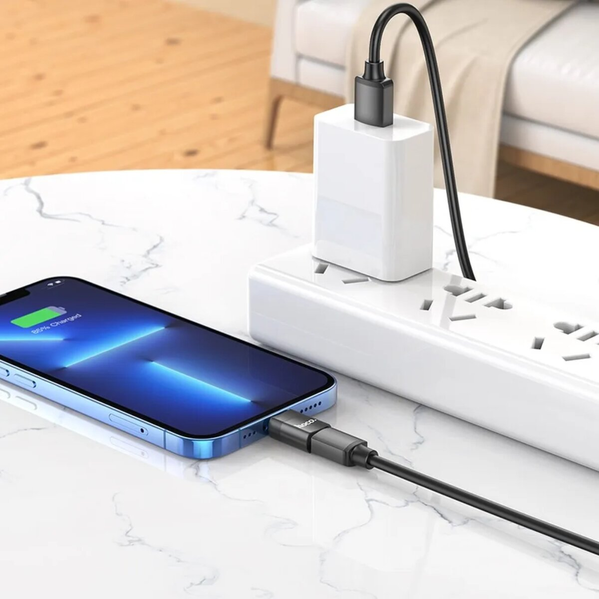 Mobiltelefon, das über ein schwarzes Kabel geladen wird. Ein weißes Ladegerät befindet sich in einer Steckdose.