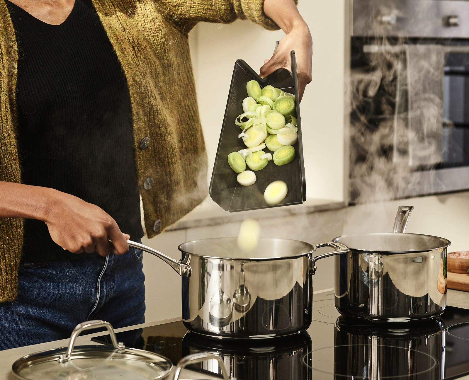 Una persona vierte verduras cortadas en una olla con agua hirviendo usando una tabla de cortar negra.