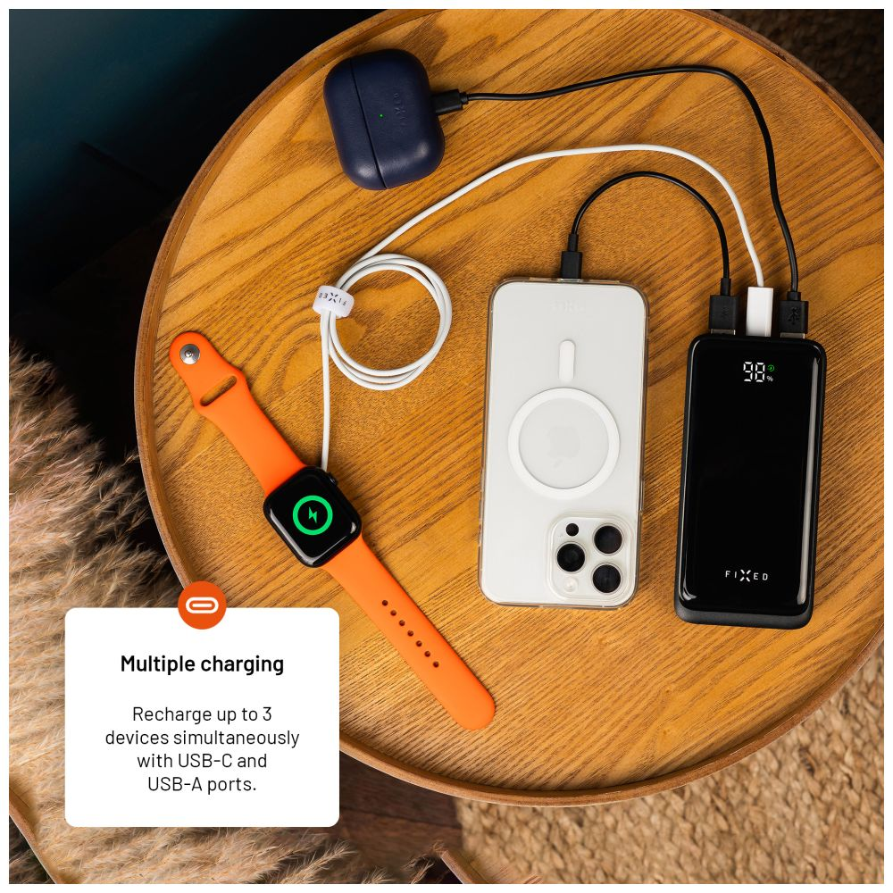 Eine Uhr, ein Telefon und eine Powerbank auf einem Holztisch, alle werden geladen.