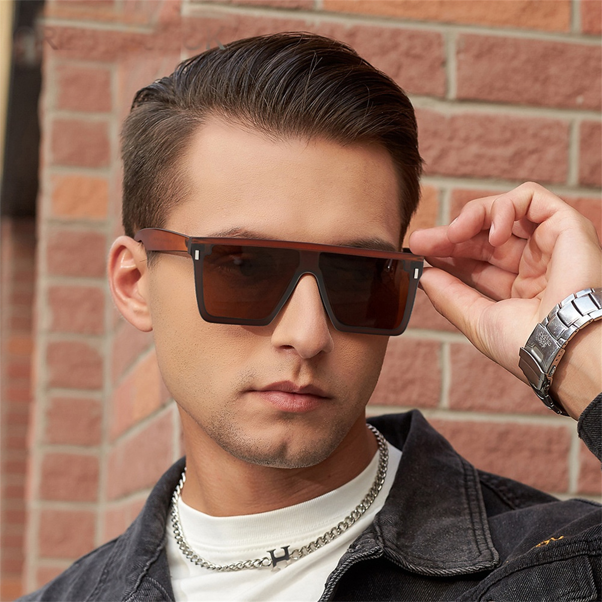Ein Mann mit brauner Sonnenbrille, schwarzer Jacke und silberner Kette, der in die Kamera blickt.