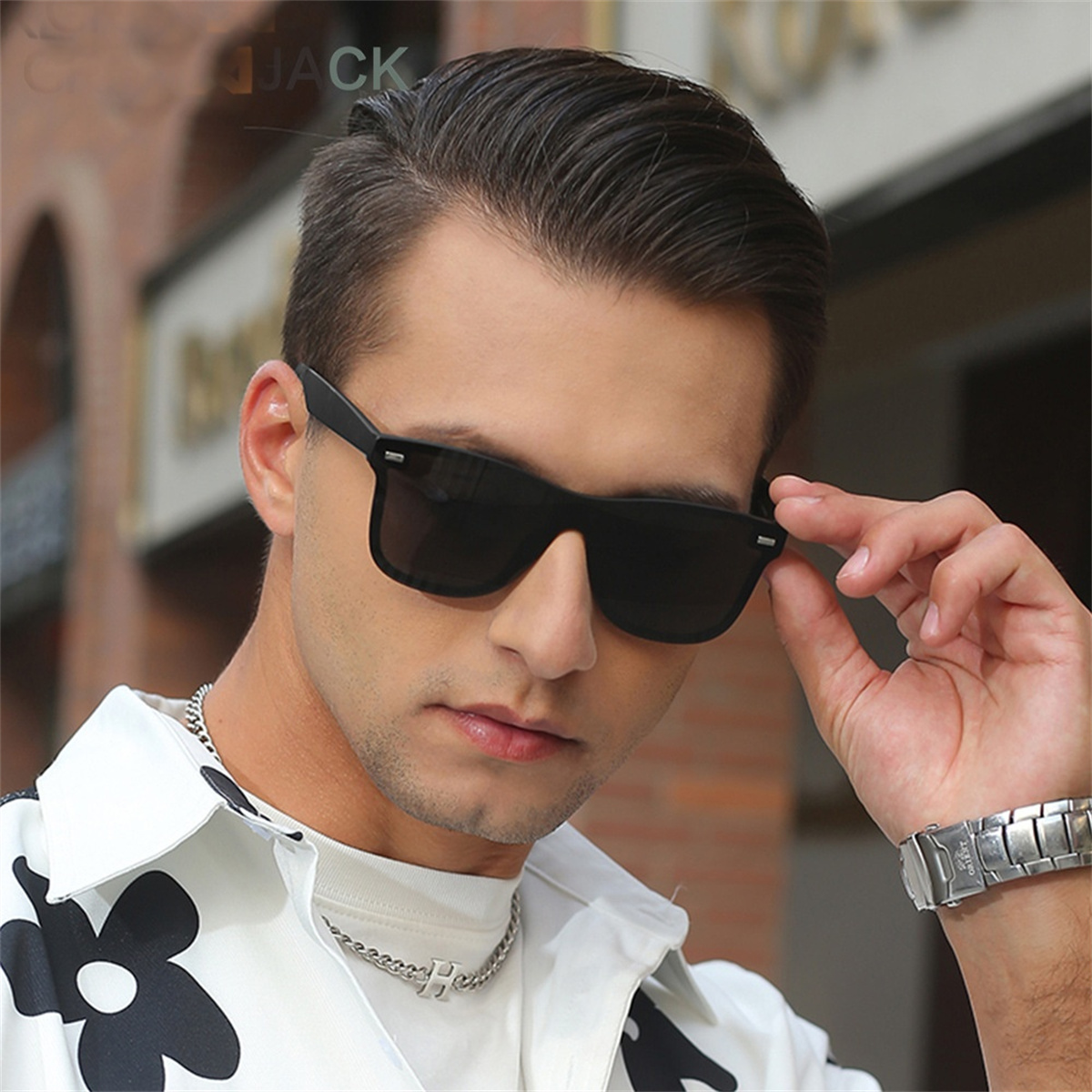 Ein Mann mit schwarzer Sonnenbrille, weißem Hemd und silberner Uhr, der in die Kamera blickt.