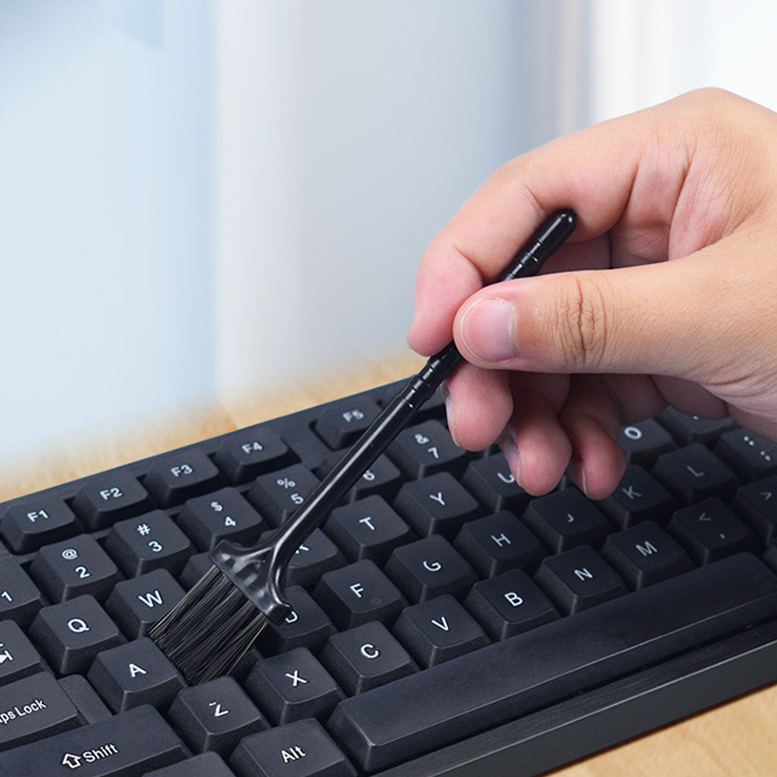Eine Hand reinigt eine schwarze Tastatur mit einem kleinen Pinsel und entfernt Staub von den Tasten.