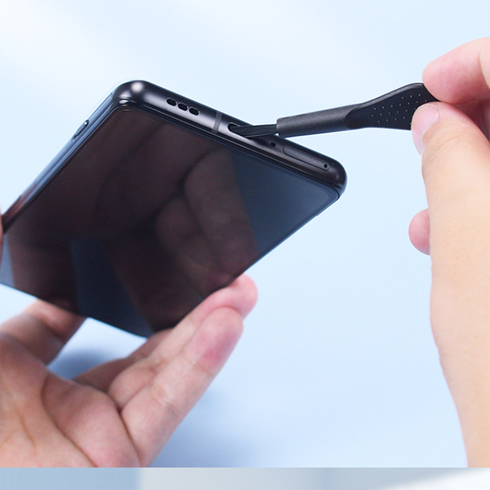 Eine Person benutzt ein Werkzeug, um etwas von einem schwarzen Smartphone zu entfernen. Blauer Hintergrund.