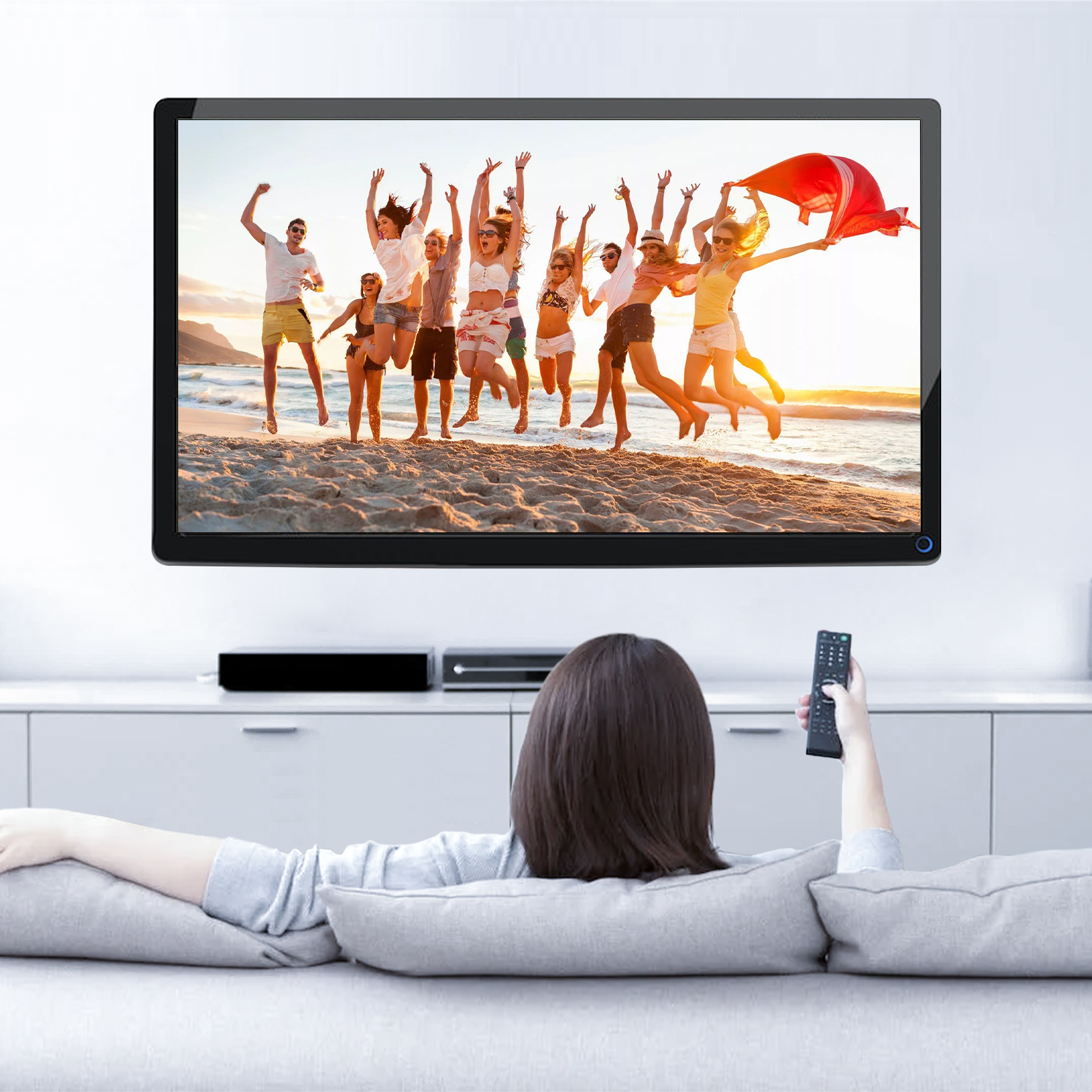 Eine Frau sieht fern, auf dem Menschen am Strand springen. Unter dem Fernseher ist eine Soundbar.