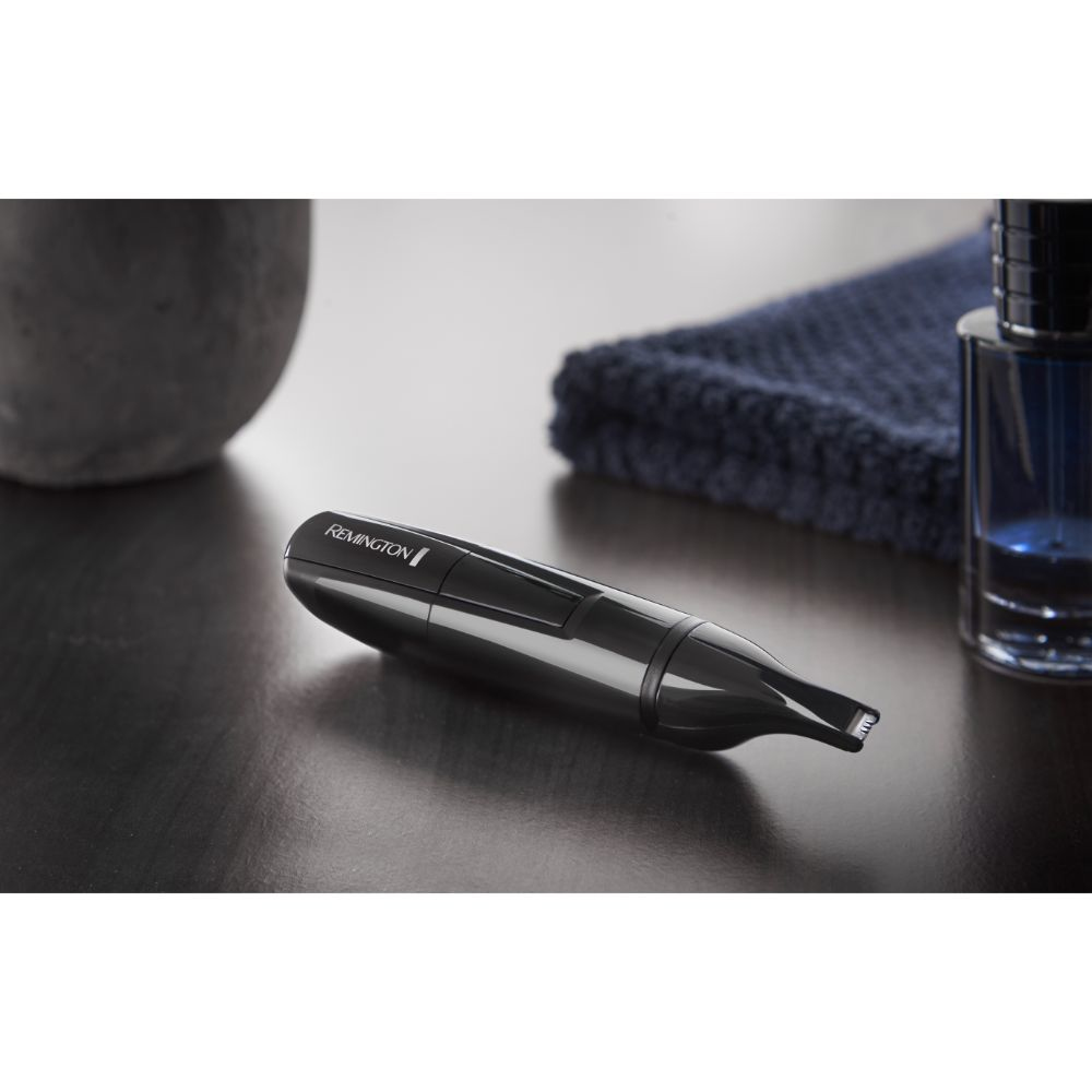 Ein schwarzer Nasenhaartrimmer auf einer Holzoberfläche, neben einer Vase und einer Parfümflasche.