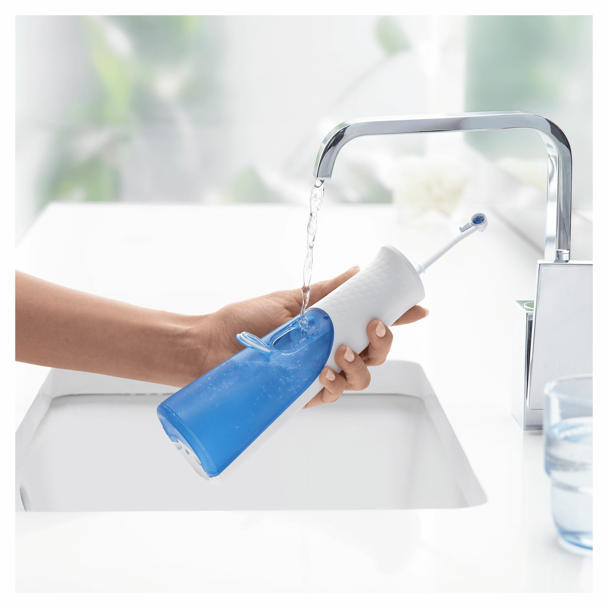 Persona llena un irrigador bucal azul y blanco con agua en un lavabo.