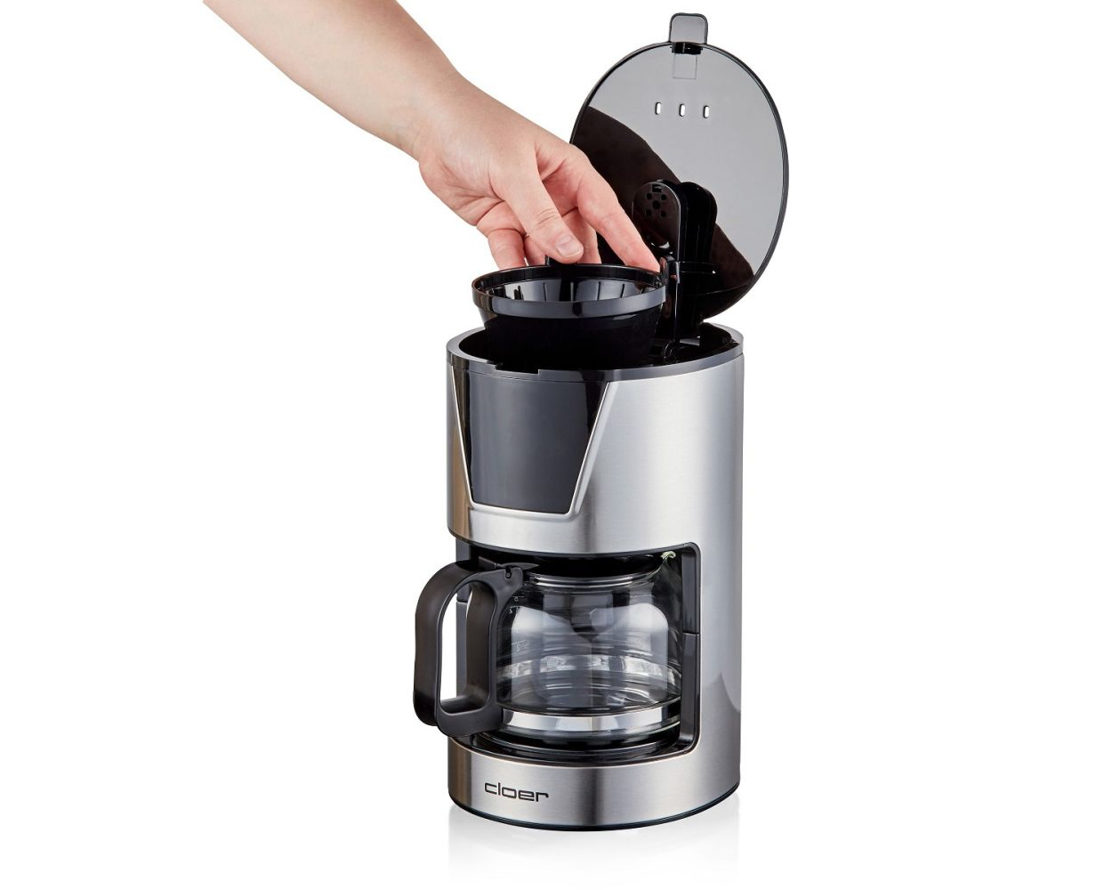Dłoń otwierająca pokrywę srebrnego ekspresu do kawy ze szklaną karafką w środku.