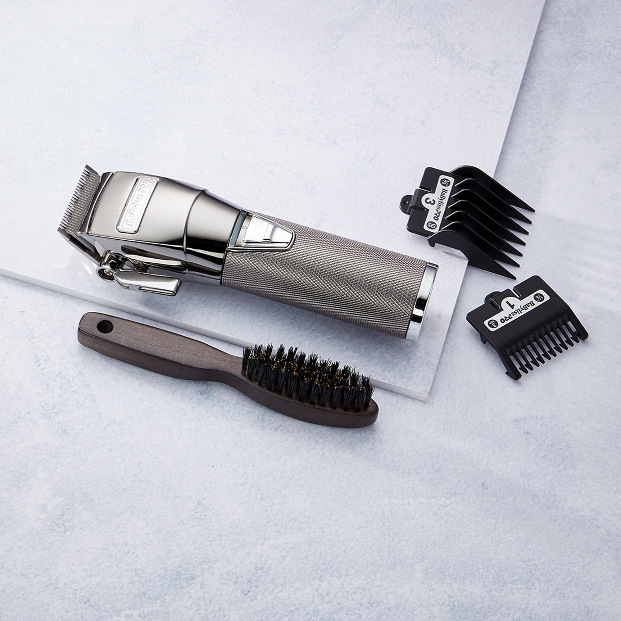 A hair clipper with attachments and a brush on a light surface. Silver hair clipper.