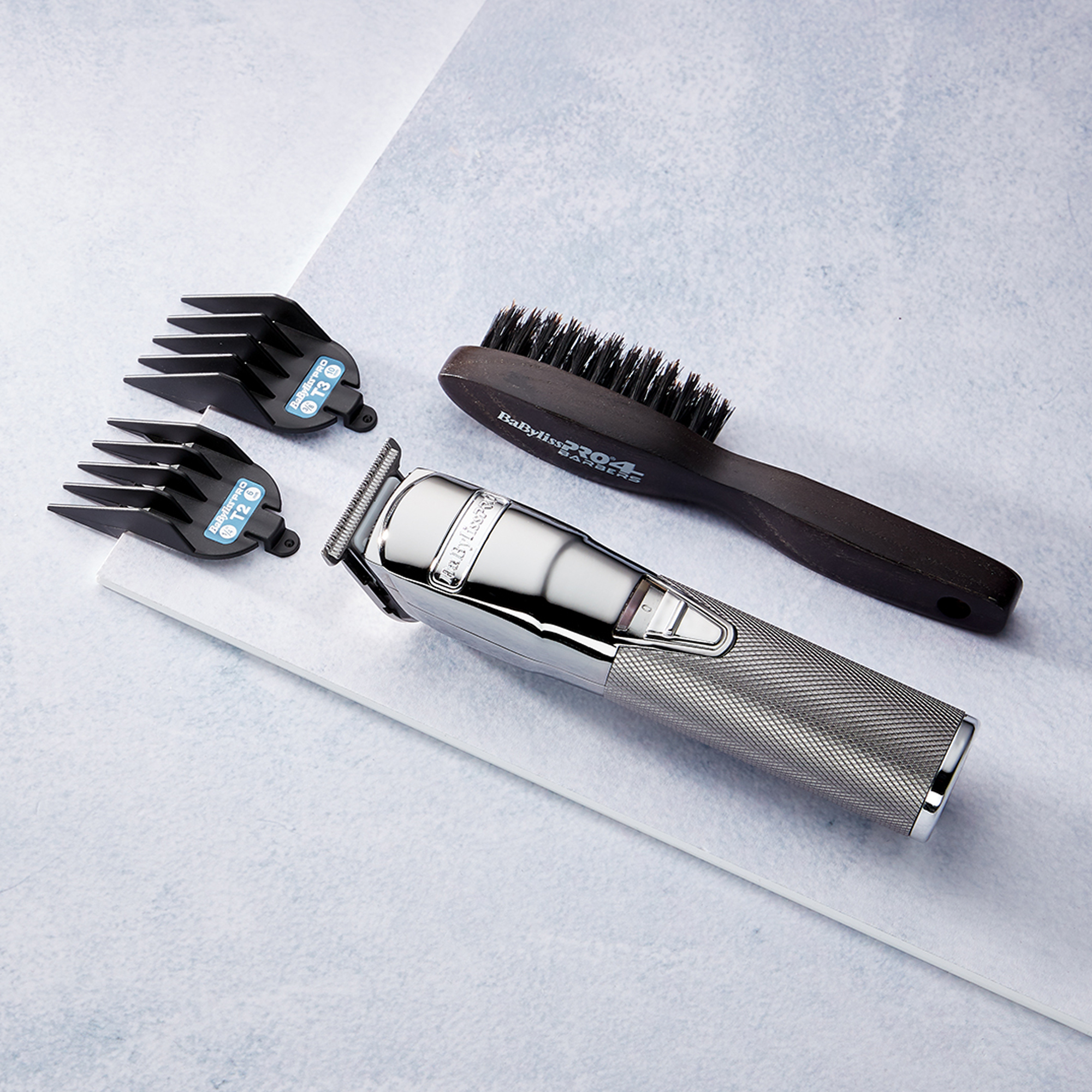 A silver hair clipper with three black attachments and a brush, on a white surface.