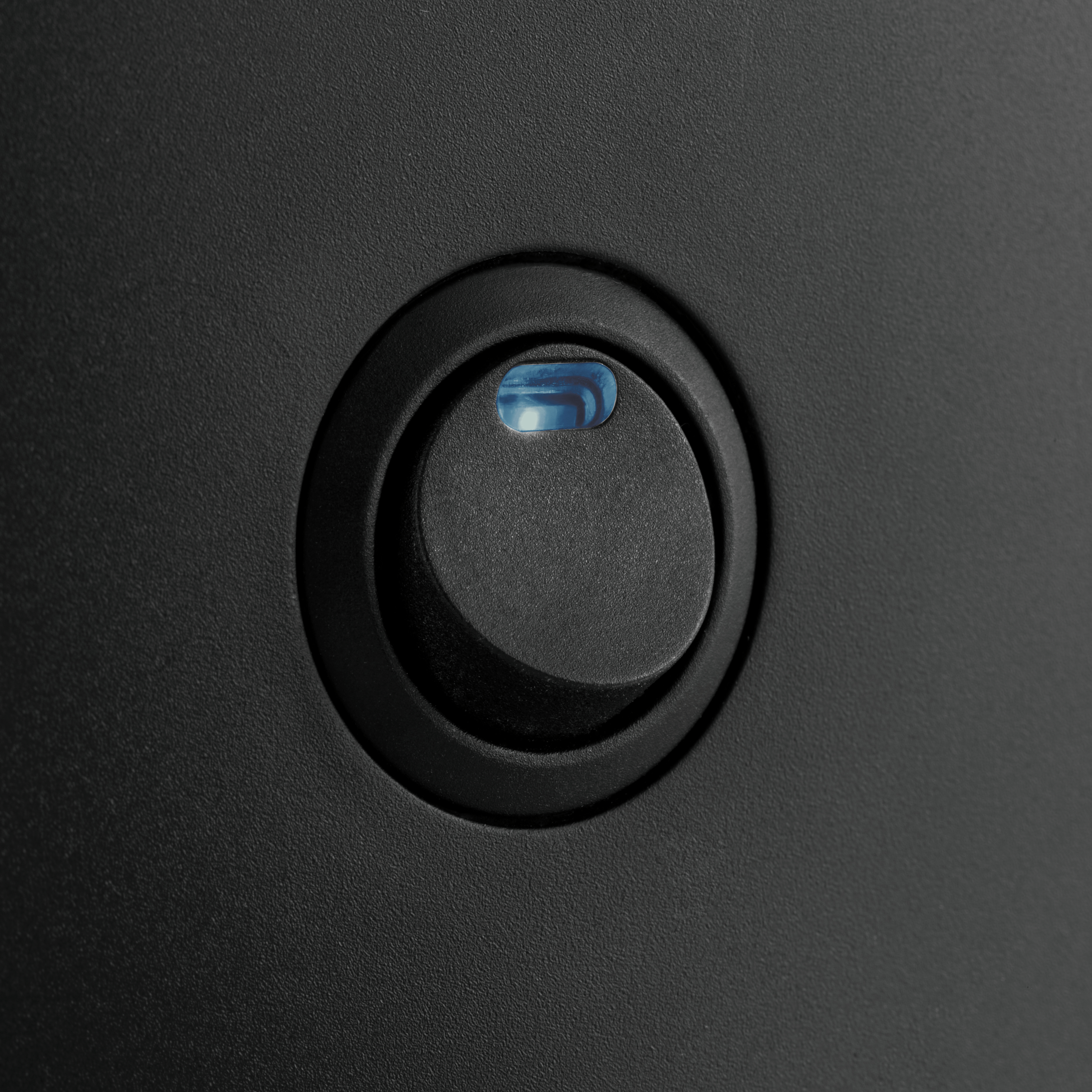 Czarna powierzchnia z okrągłym przyciskiem. Przycisk ma niebieskie światło.