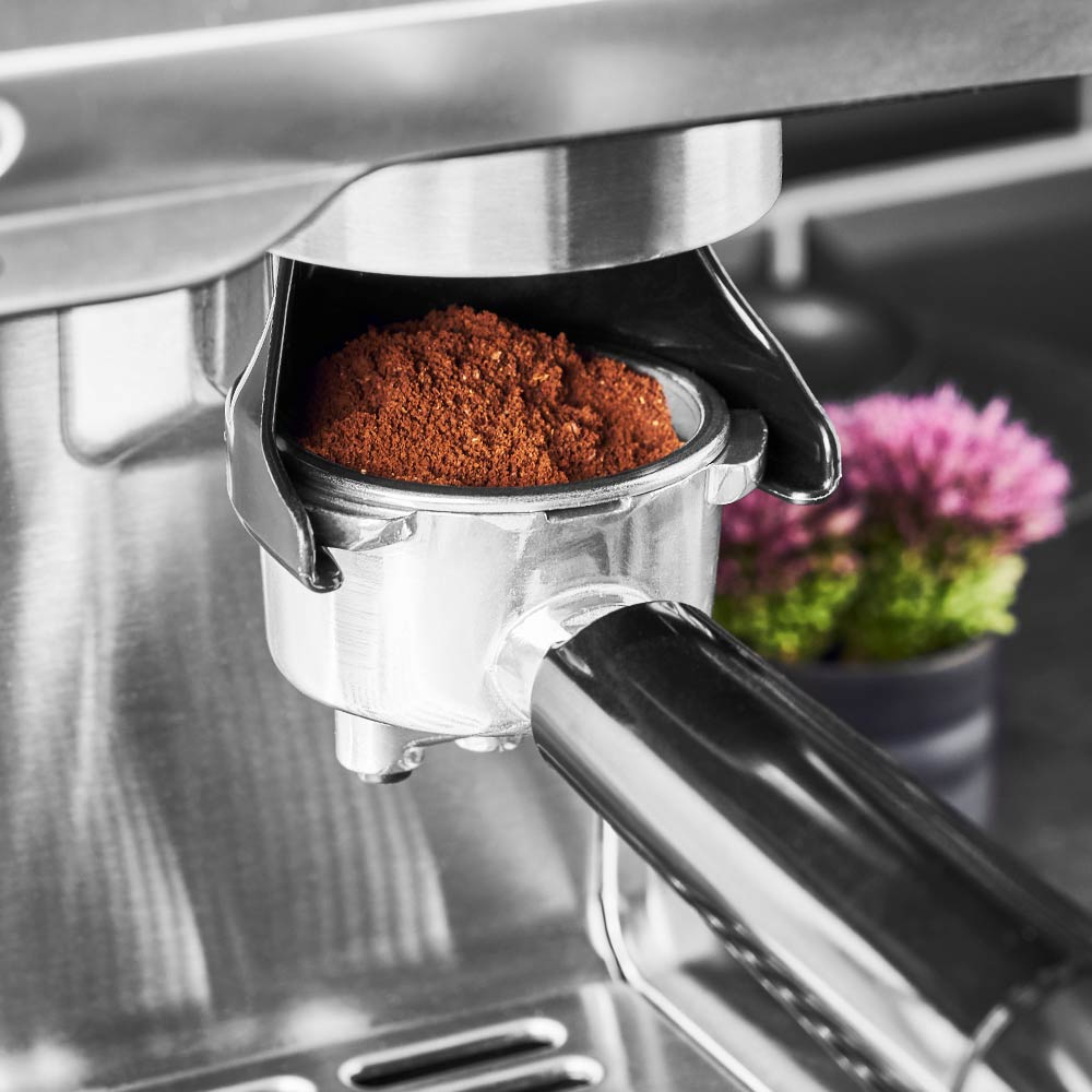 Ekspres do kawy z mieloną kawą w kolbie, kwiaty w tle.