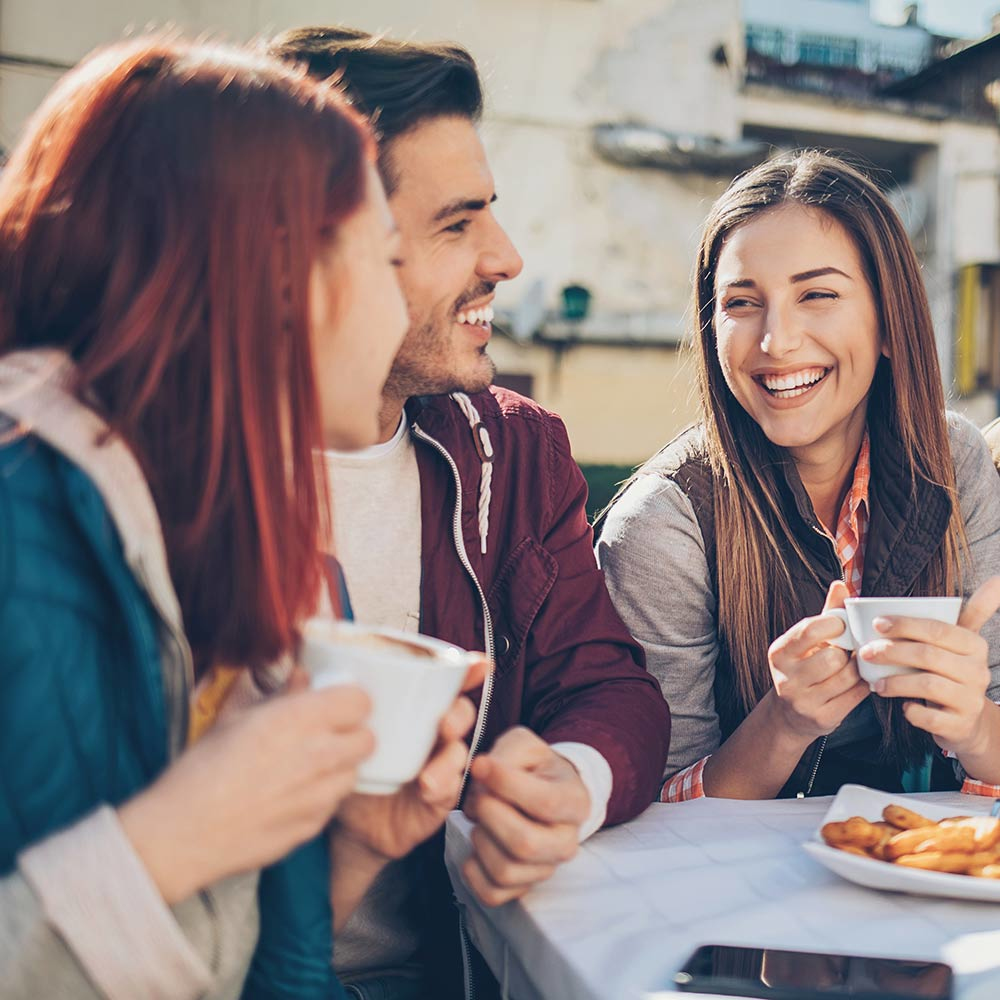 Tre persone ridono e bevono caffè a un tavolo all'aperto.