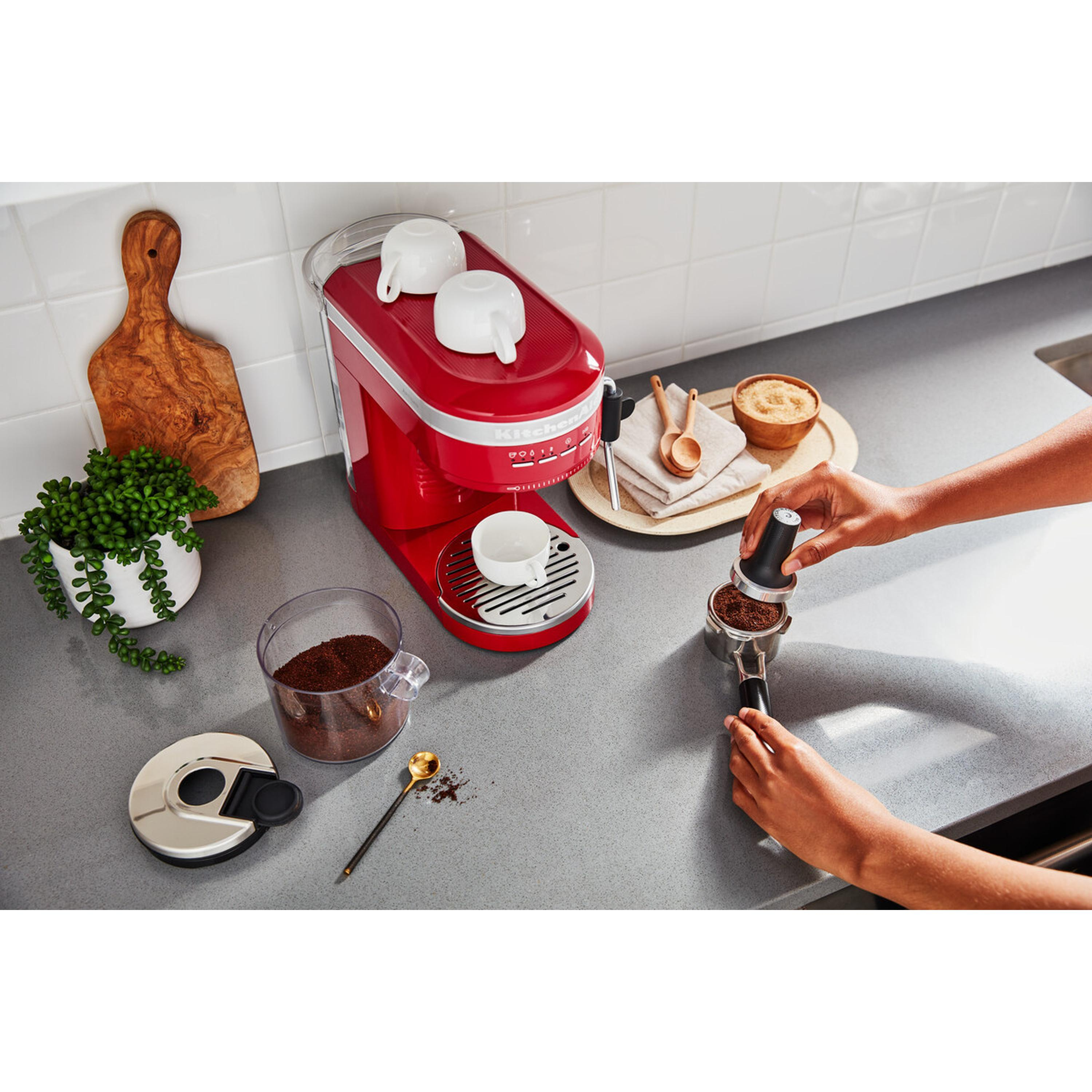 Rote Espressomaschine mit Tassen, Kaffee und Händen einer Person.