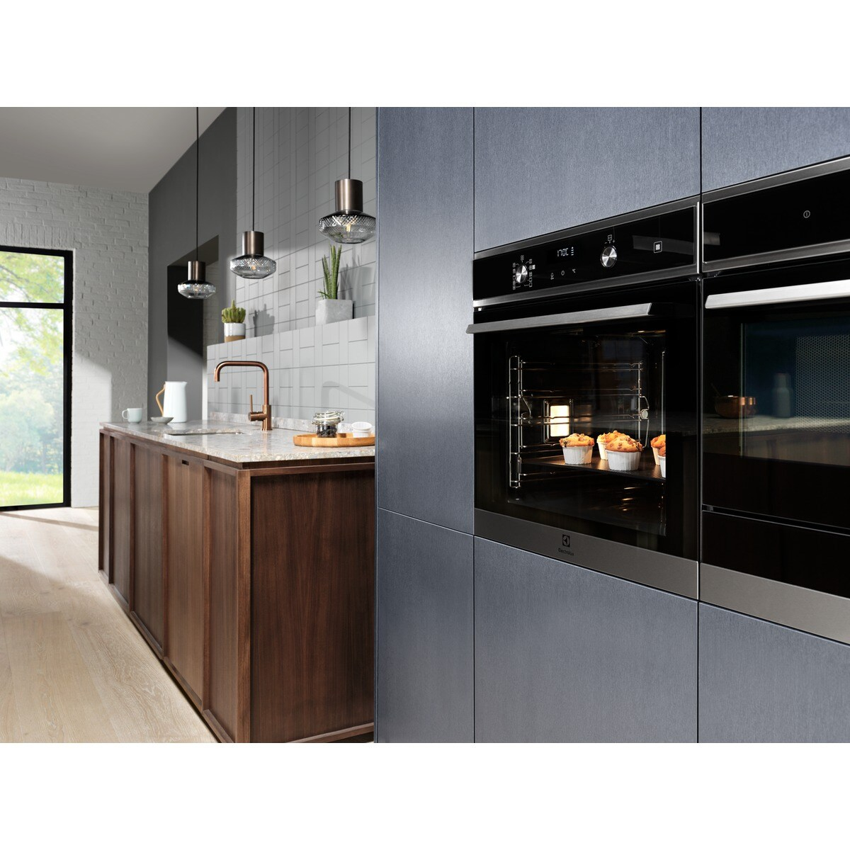 Cucina con forno. Il forno mostra muffin. Dietro armadi in legno e luci sospese.
