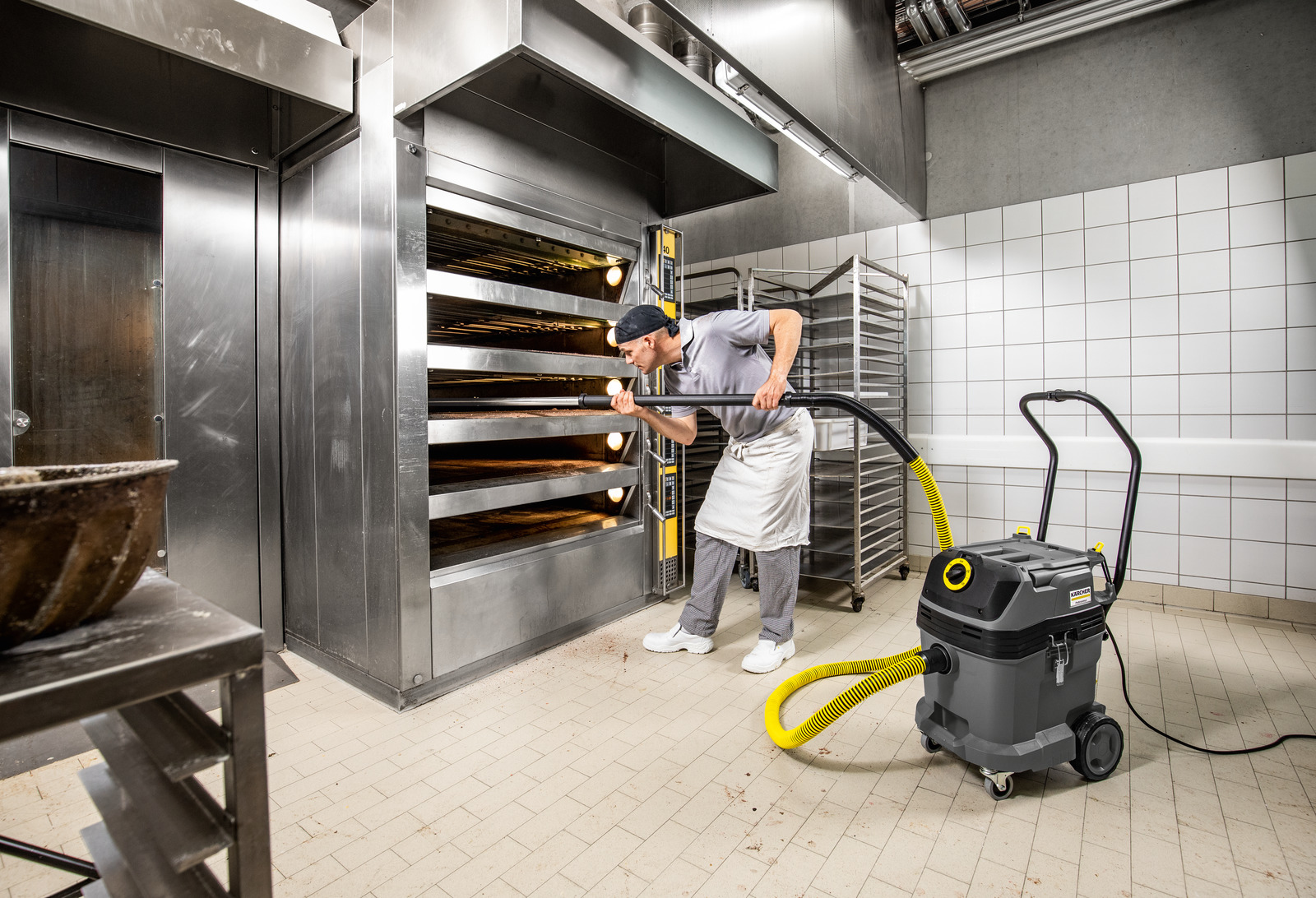 Mężczyzna w kuchni używa odkurzacza z żółtym wężem w pobliżu piekarnika.