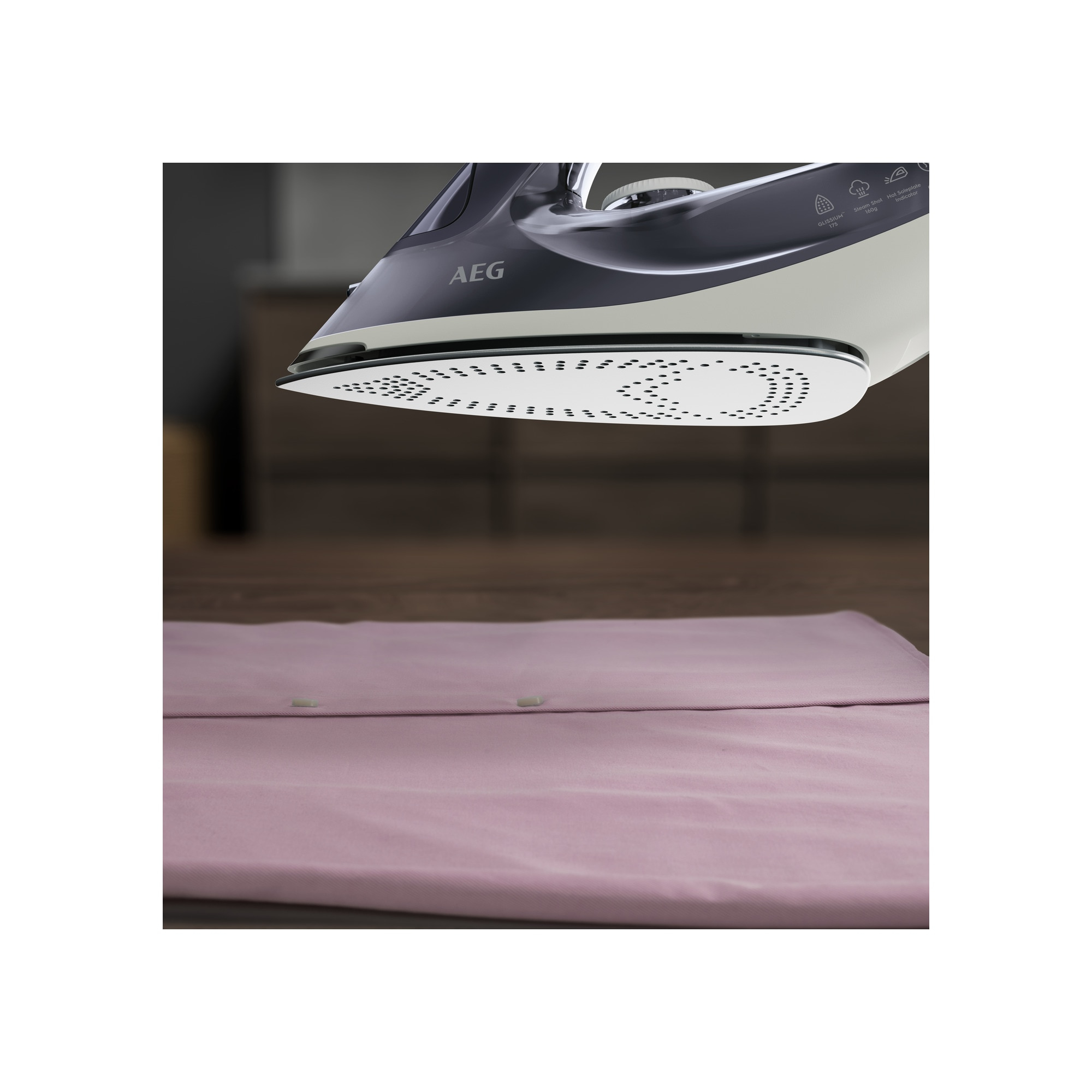 Żelazko AEG, z białą stopą, prasujące różową koszulę na drewnianej powierzchni.