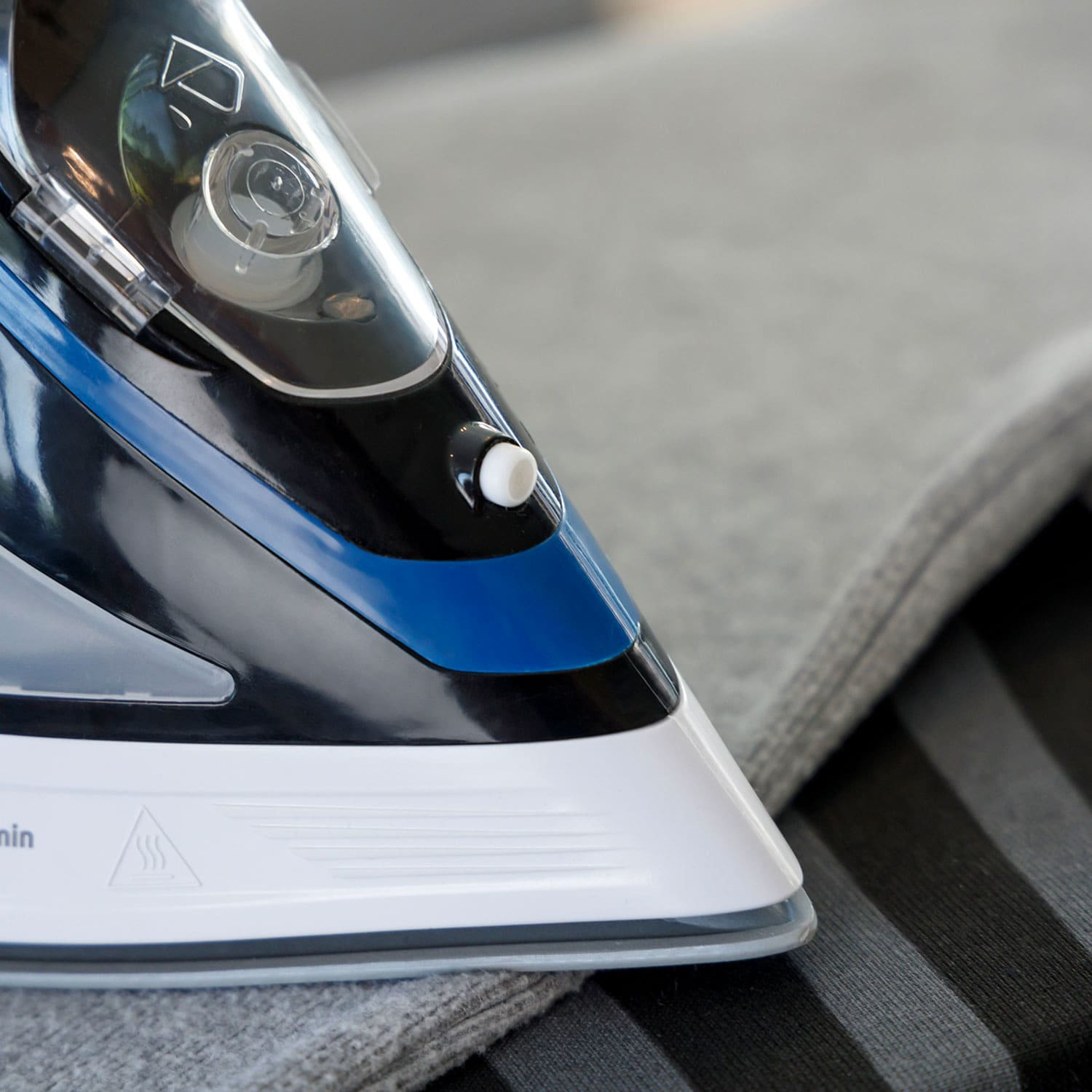 Żelazko na szarej tkaninie, zbliżenie z czarnymi, niebieskimi i białymi detalami.