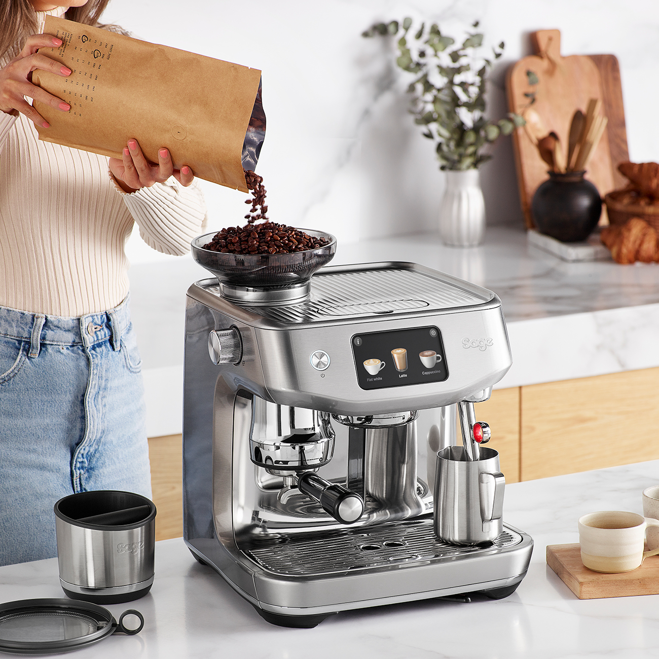 Una persona versa chicchi di caffè in una moderna macchina per espresso argentata.
