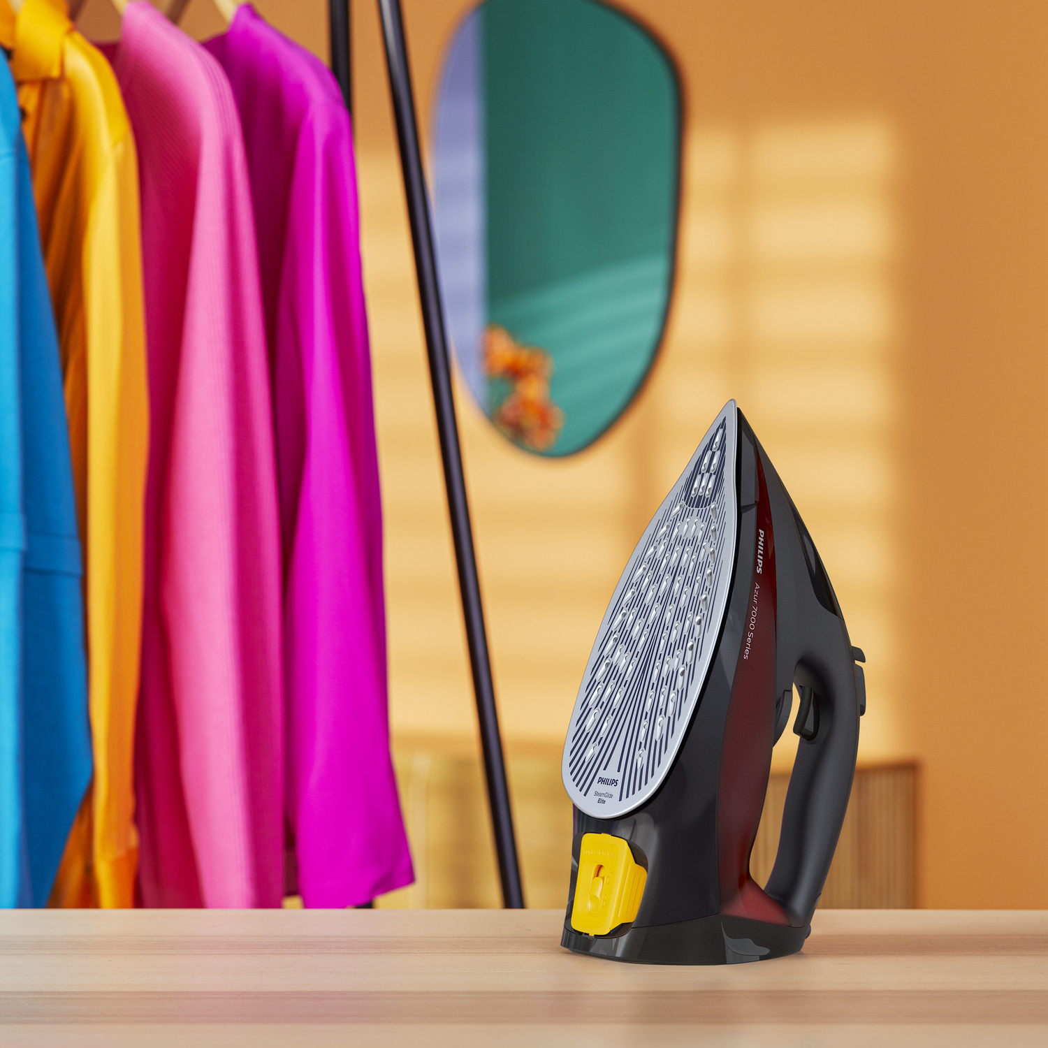 Czarno-czerwone żelazko na drewnianej powierzchni przed kolorowymi ubraniami.