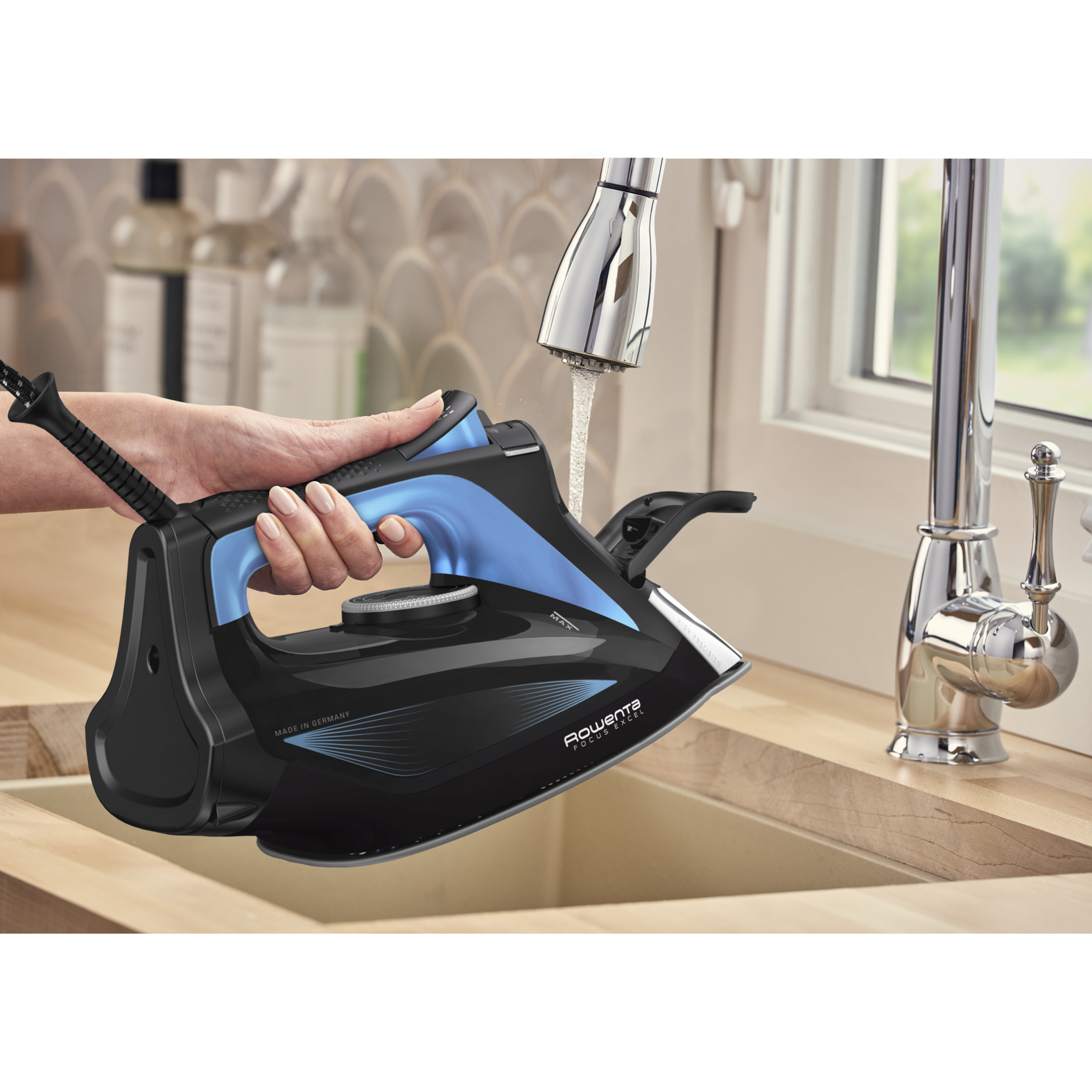 Żelazko napełniane wodą w zlewie. Niebieskie, czarne i chromowane detale.