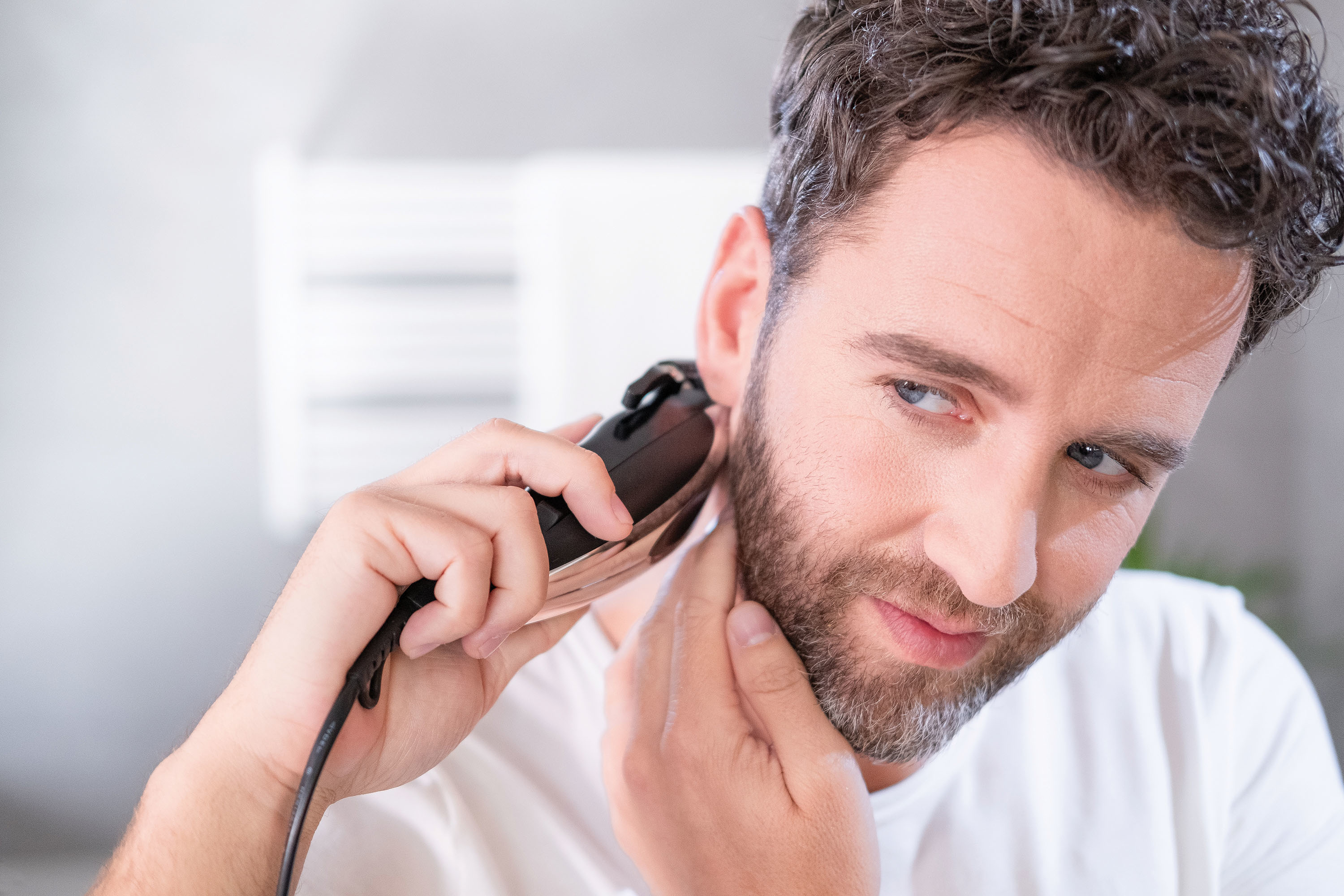 Mężczyzna goli brodę golarką elektryczną, patrząc w lustro.