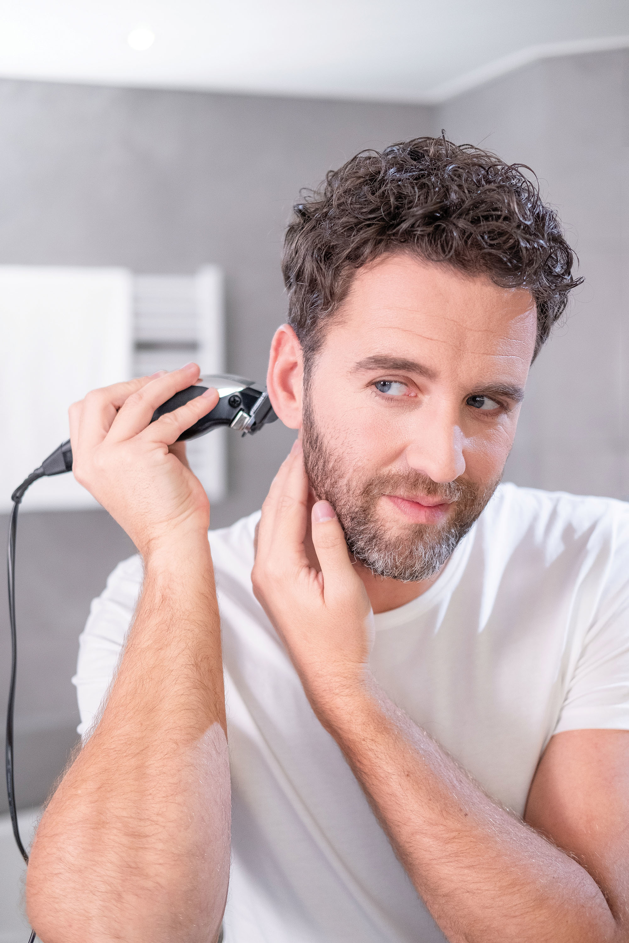 Mężczyzna goli szyję golarką elektryczną, patrząc w bok.