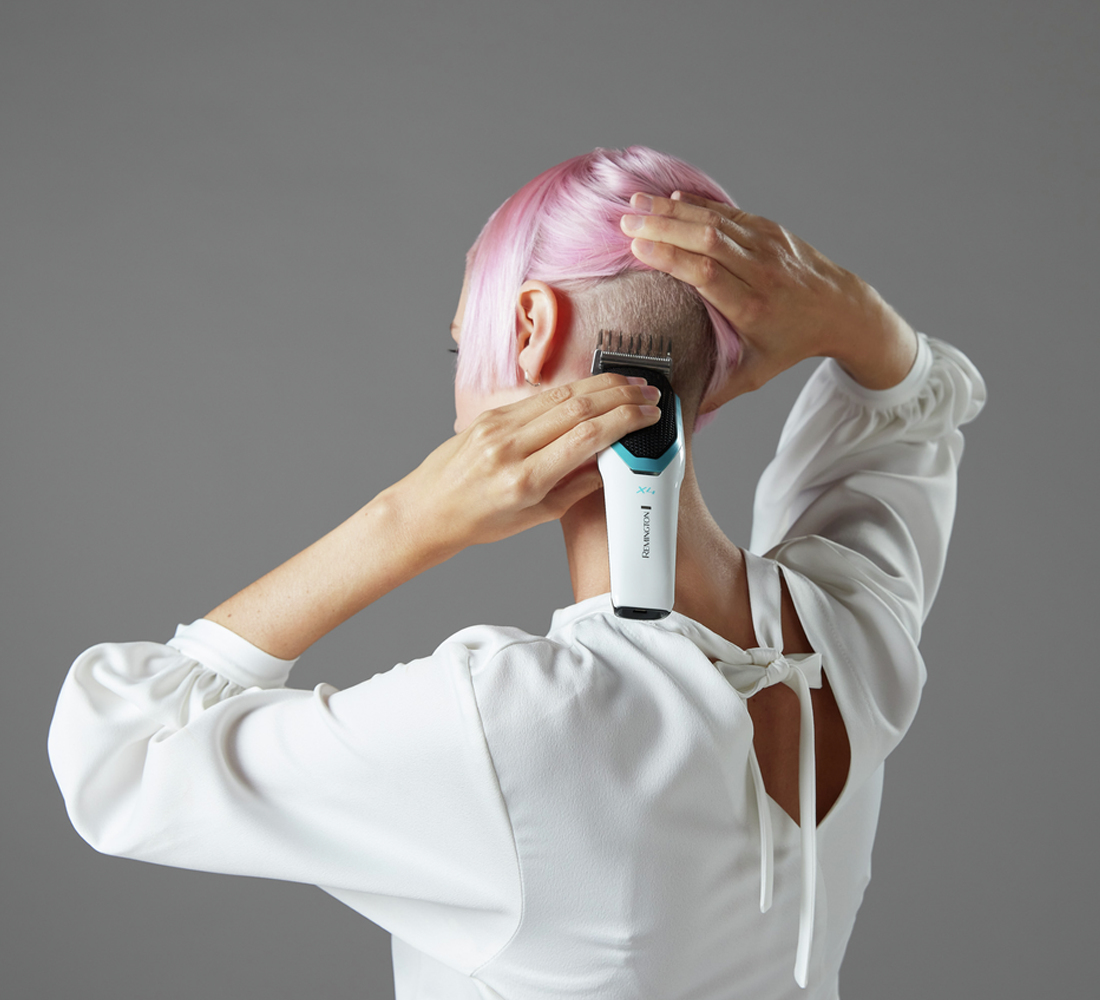 Una donna con i capelli rosa si rade la nuca con un rasoio elettrico.