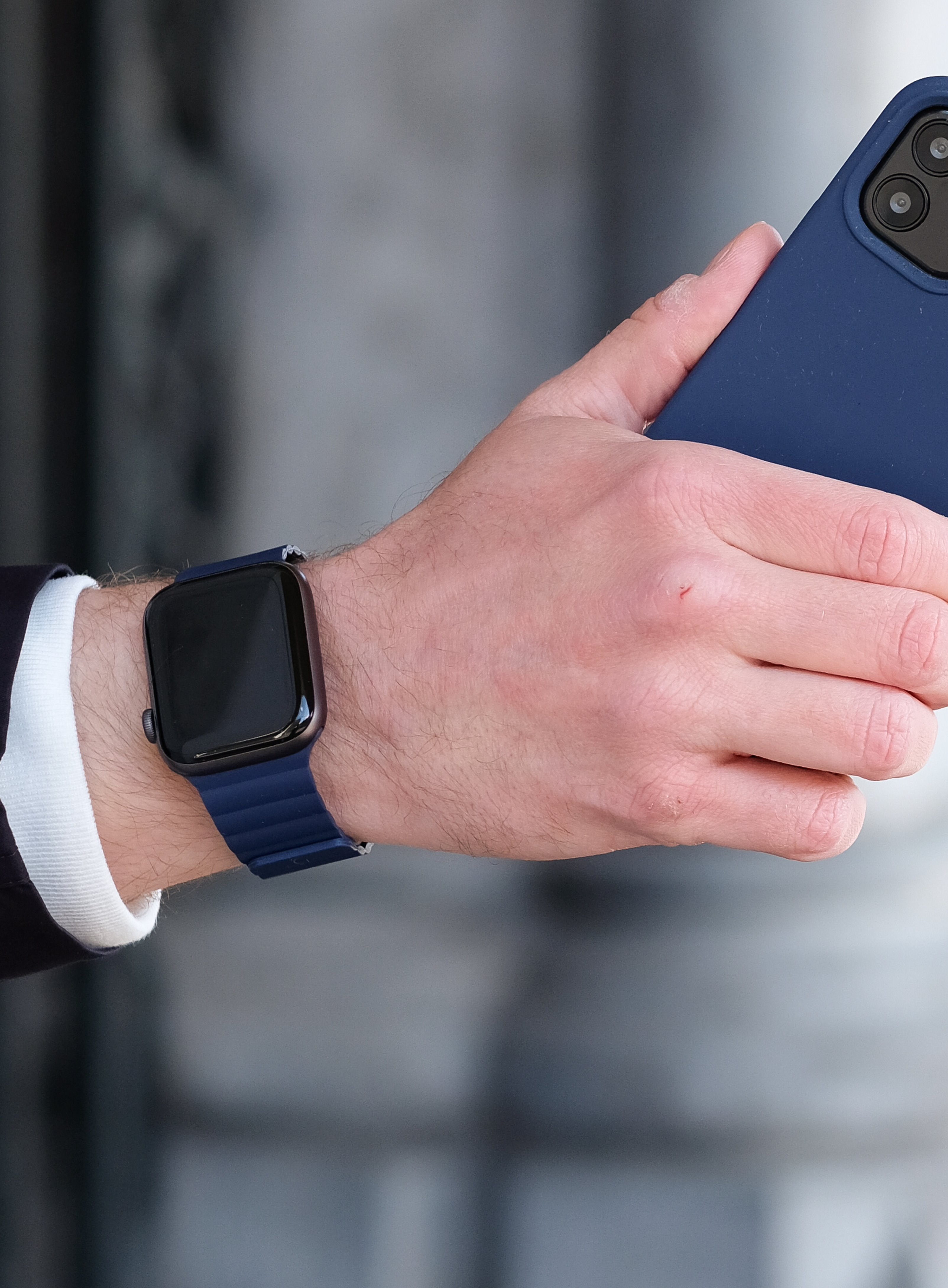 Osoba nosząca Apple Watch, ciemnoniebieski pasek, trzymająca niebieski telefon.