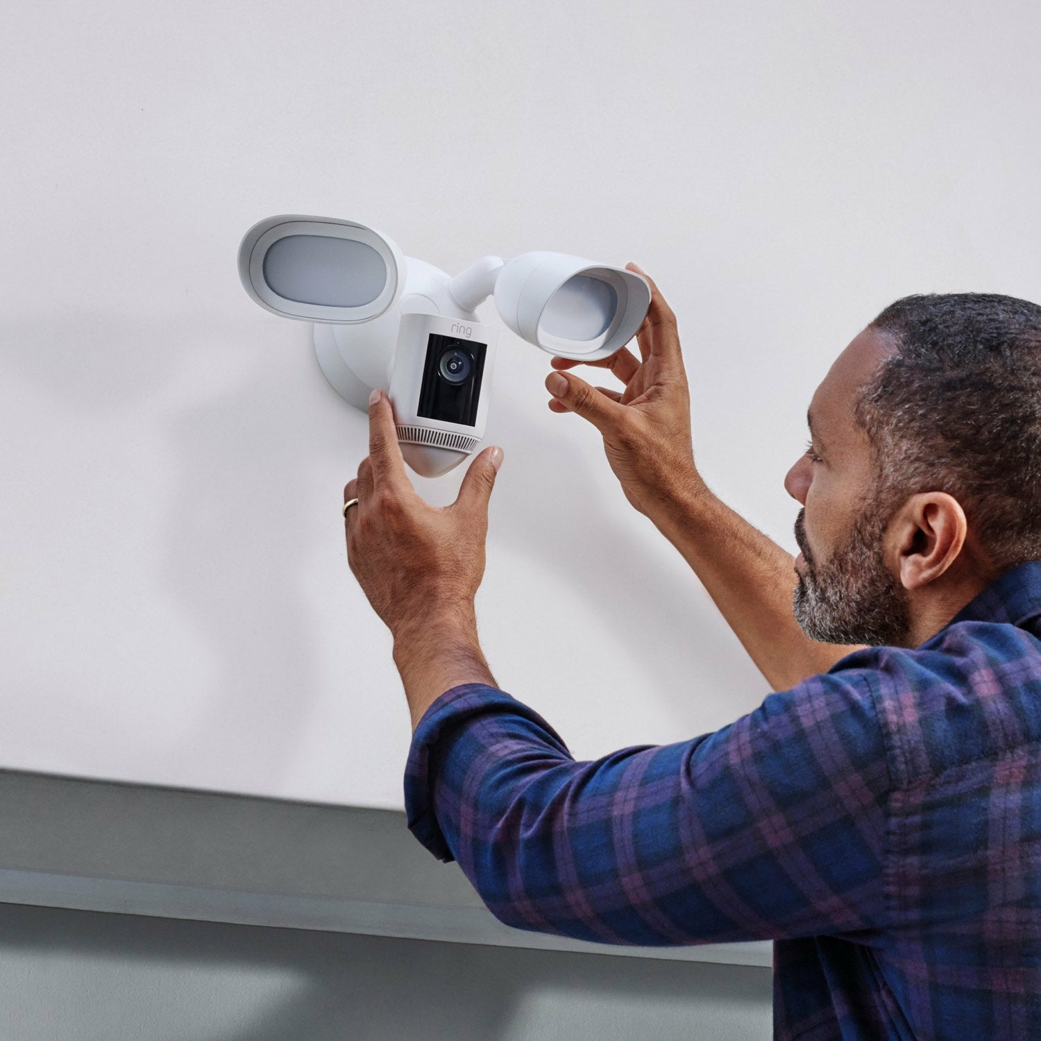 Mężczyzna instalujący białą lampę bezpieczeństwa z kamerą na białej ścianie. Lampa ma dwie lampy.