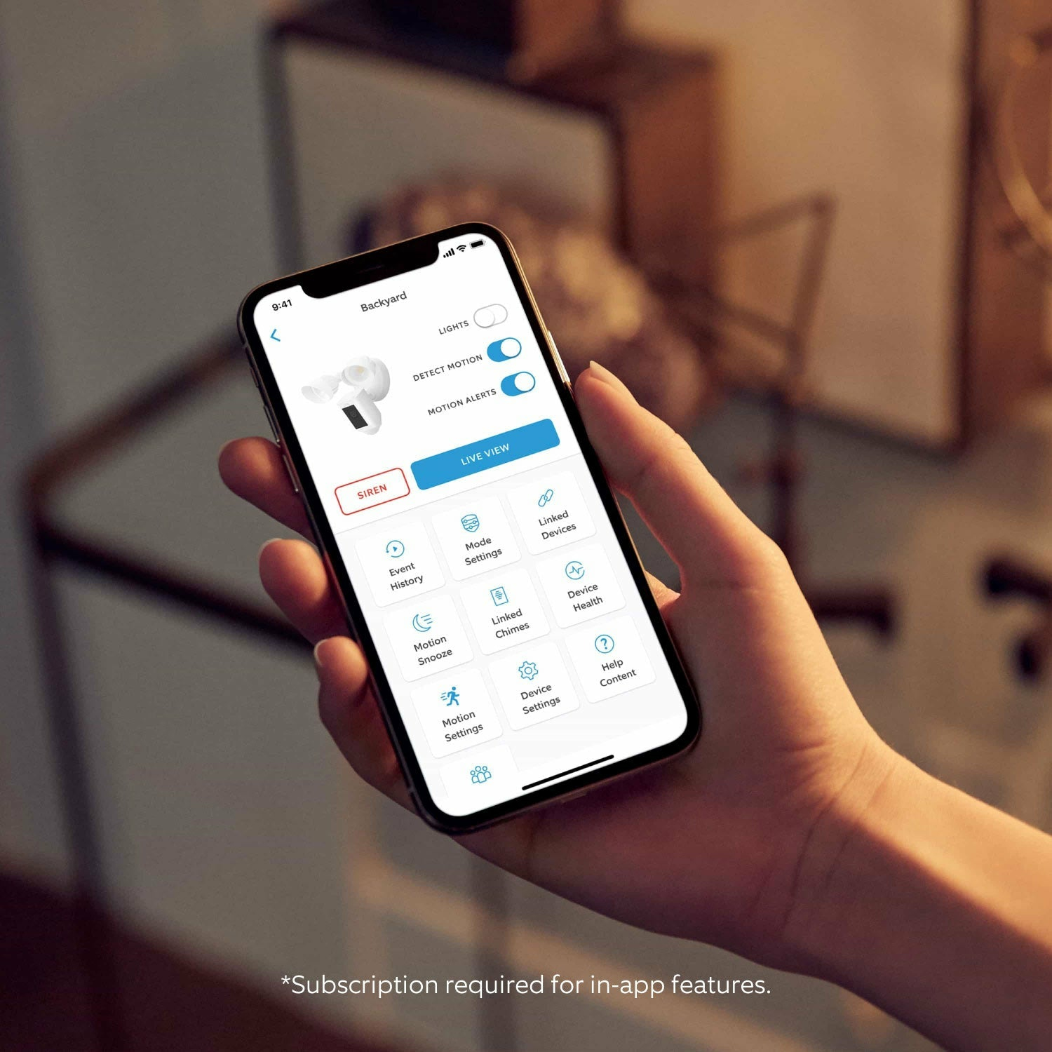 Dłoń trzymająca smartfona z ekranem aplikacji. Pokazuje widok podwórka i funkcje aplikacji.