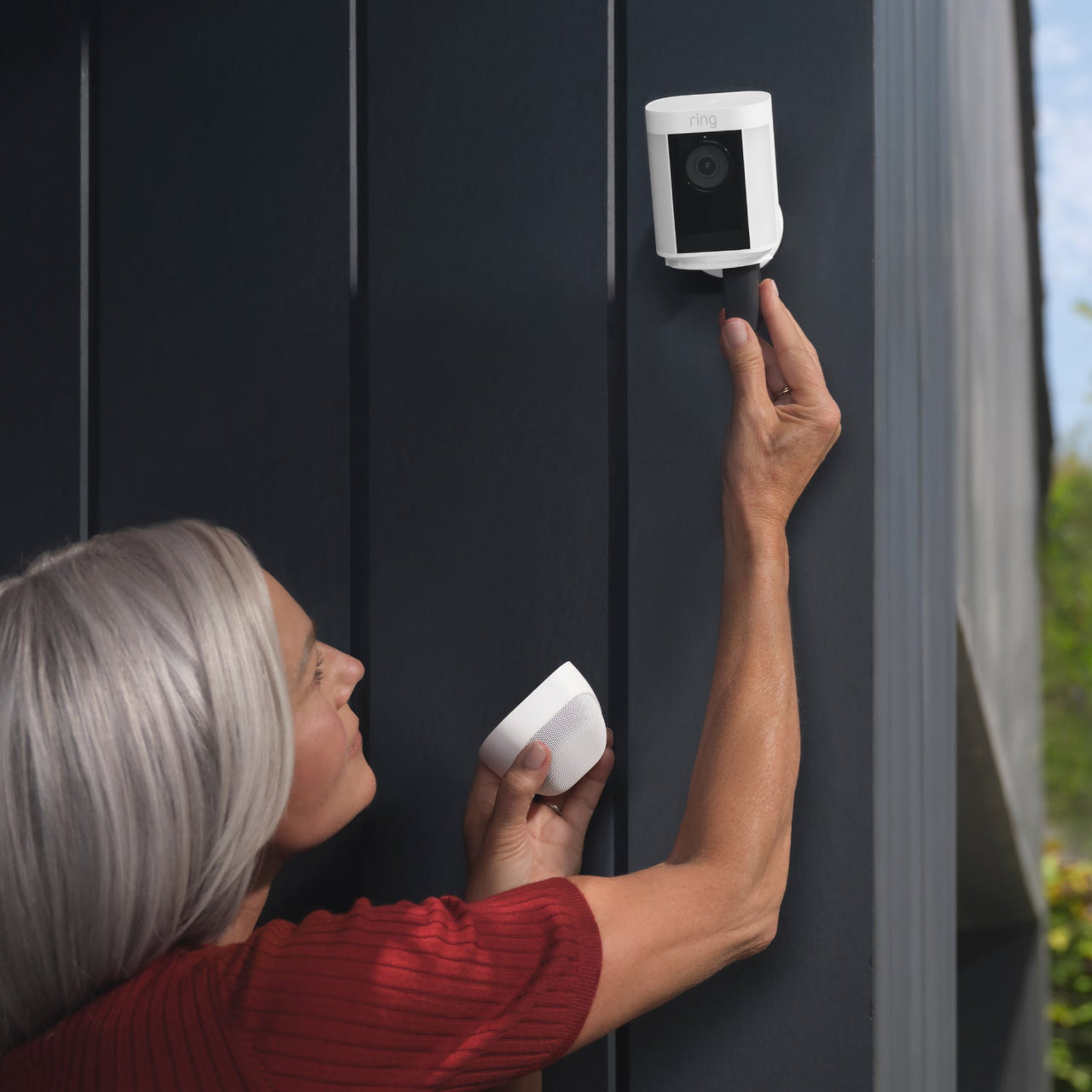 Kobieta instalująca białą kamerę bezpieczeństwa Ring na ciemnoszarej ścianie.
