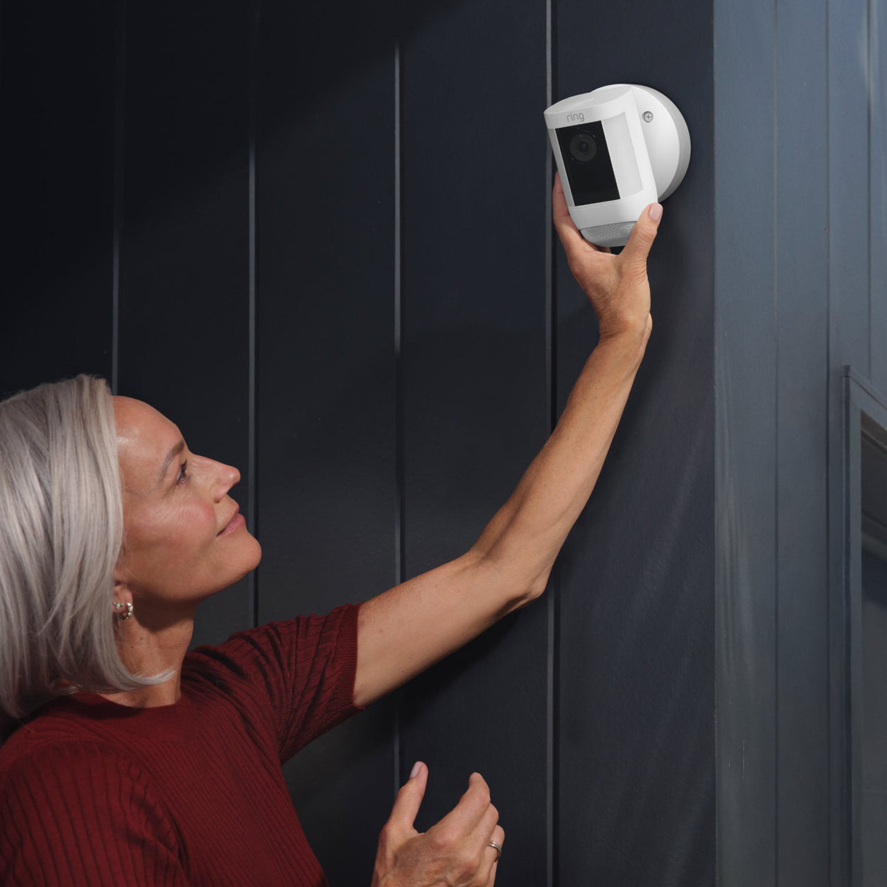 Kobieta instaluje kamerę bezpieczeństwa na ścianie, czerwony top, ciemna ściana.