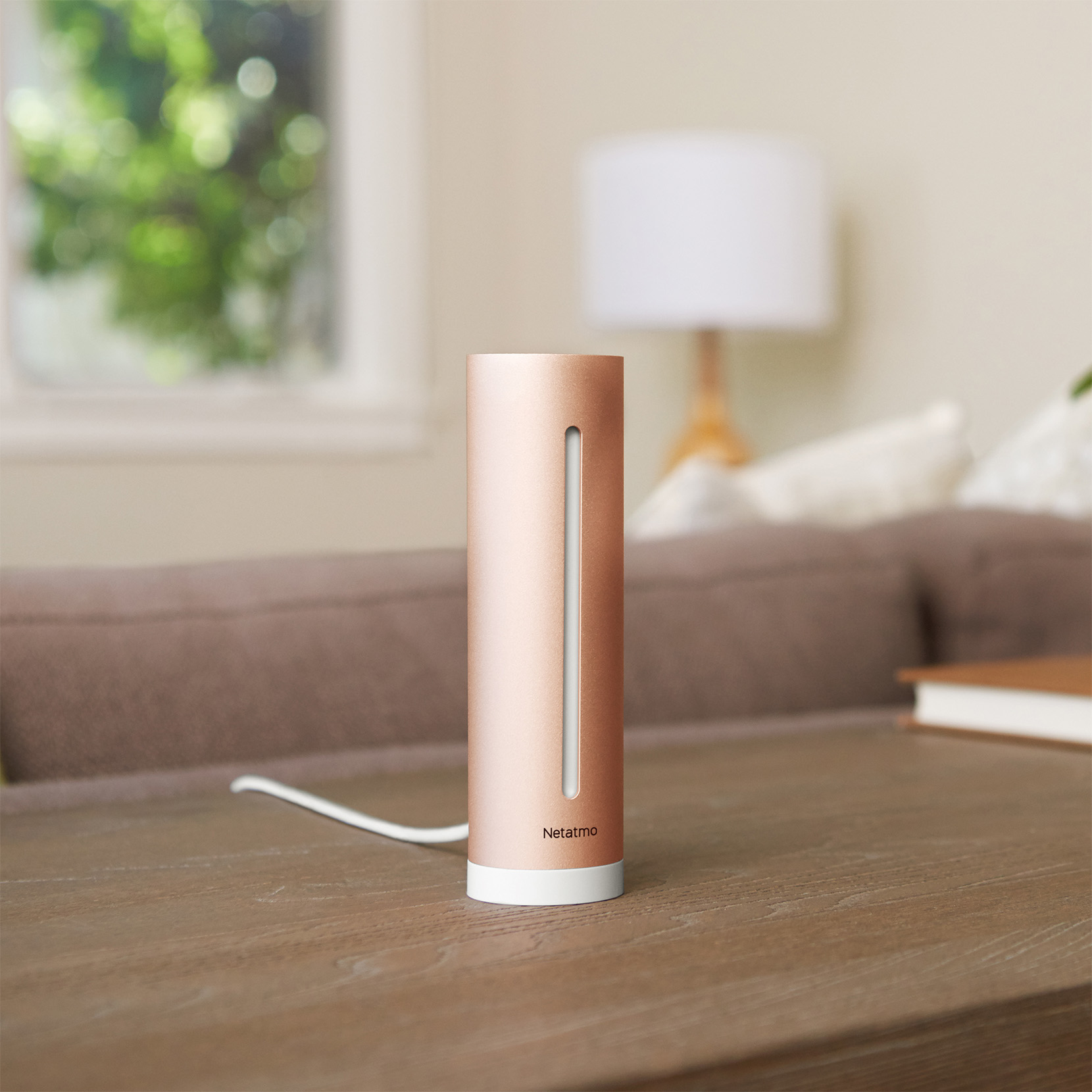 A rose gold smart home device on a wooden table with a white cord.