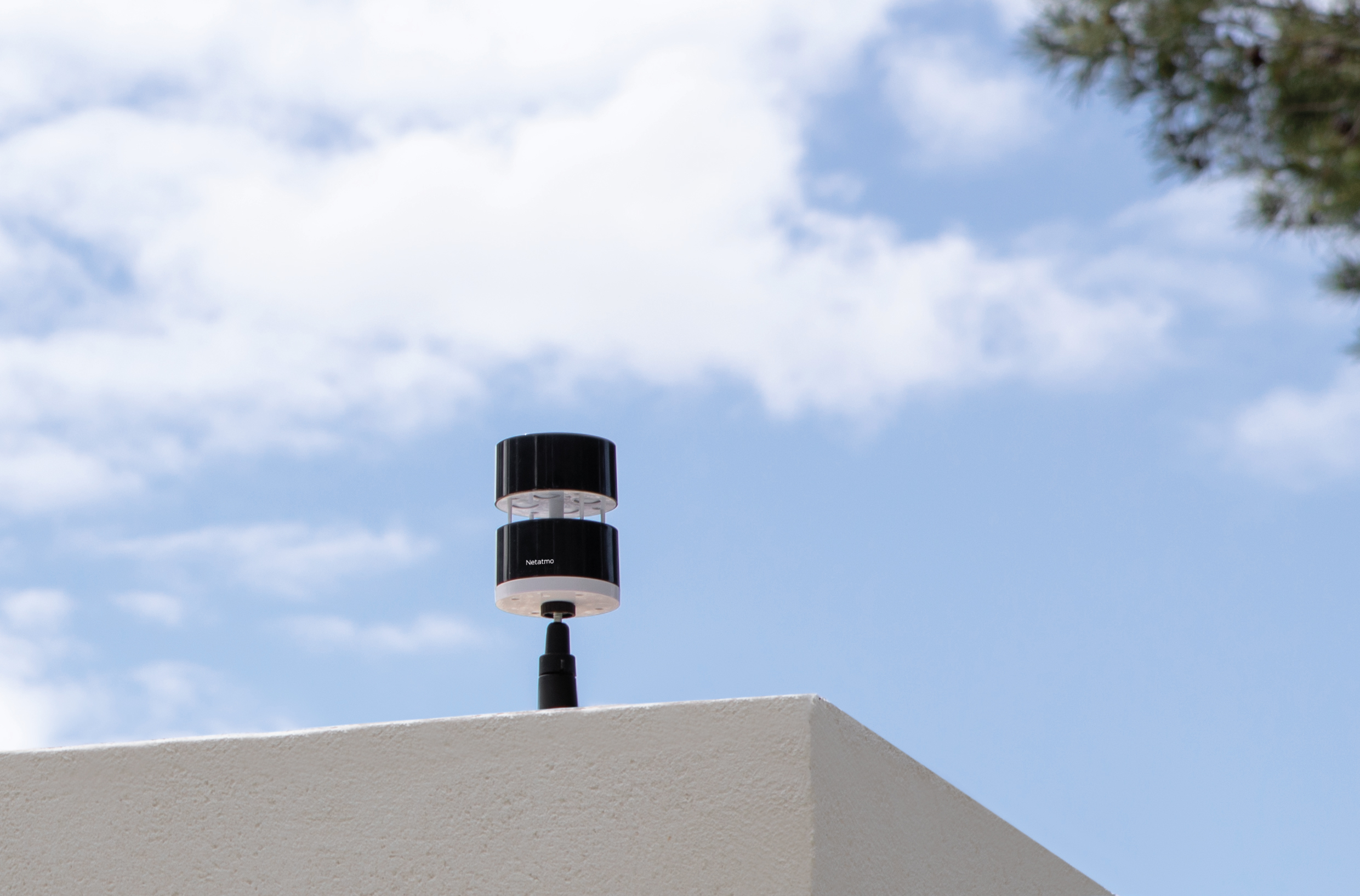 A smart anemometer on a white surface, with blue sky and clouds in the background.