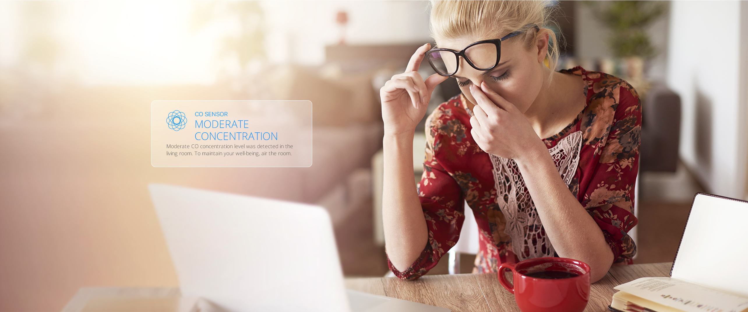 Kobieta przy biurku z laptopem, okularami i czerwonym kubkiem. Tekst: czujnik CO, umiarkowane stężenie.