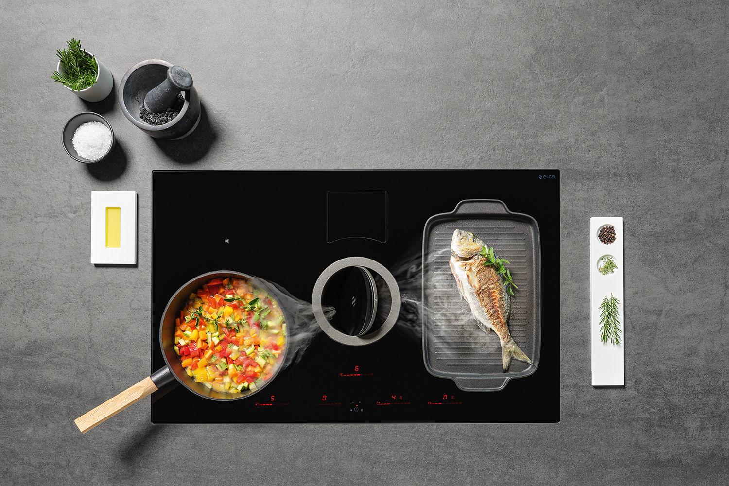 Płyta grzewcza z warzywami i rybą, ziołami i akcesoriami na szarej powierzchni.