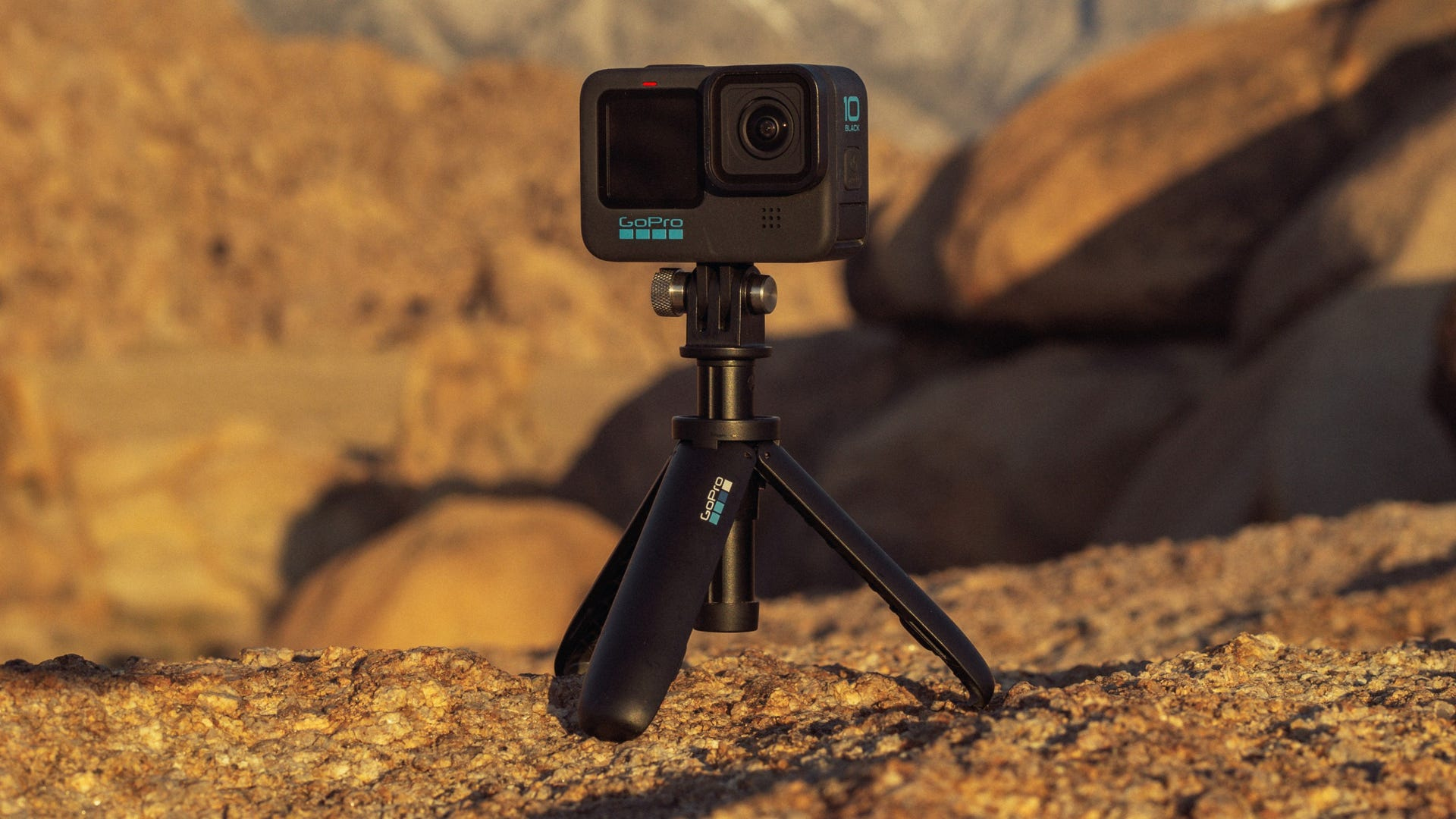 Una cámara GoPro negra en un trípode, sobre un fondo natural, tipo desierto.