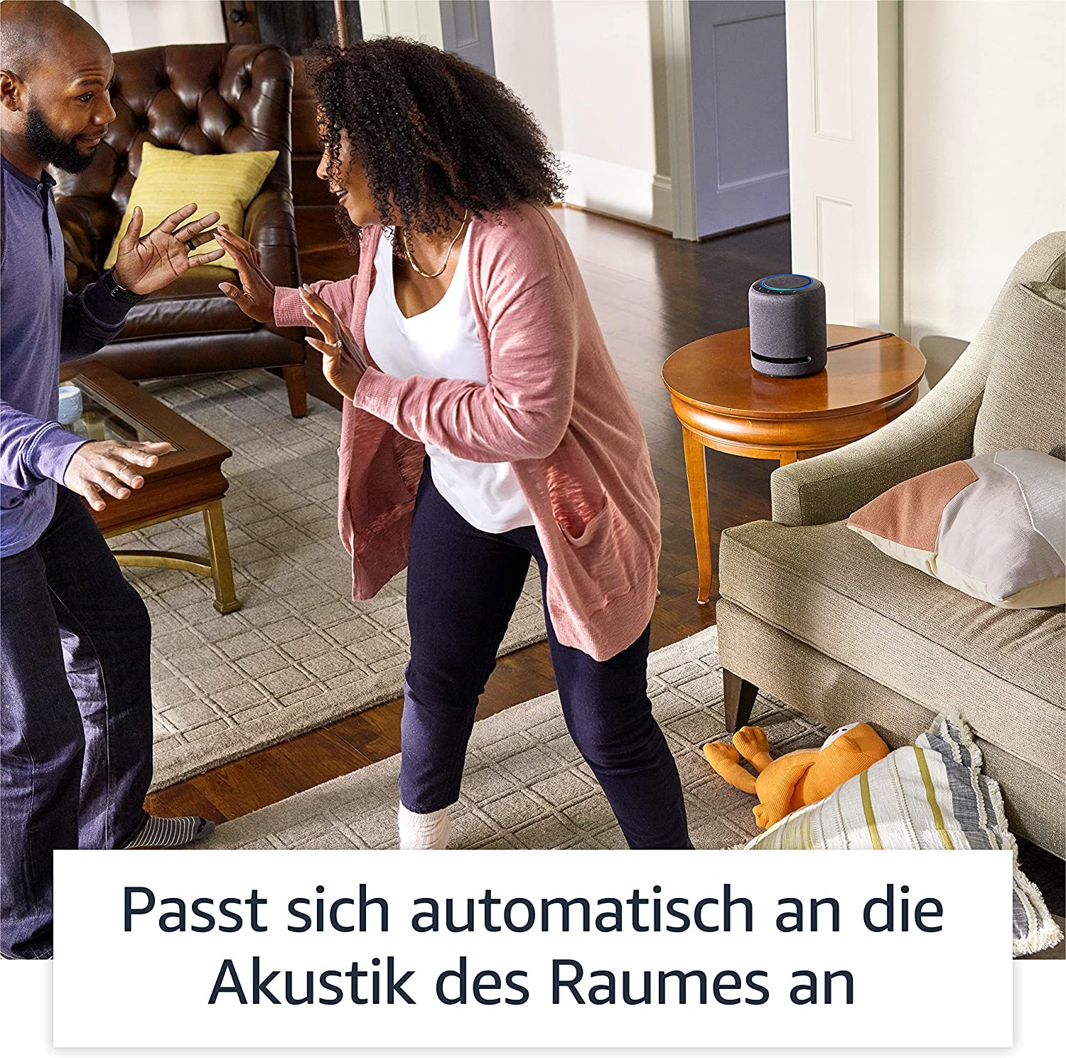 Personen interagieren mit einem Smart Speaker. Text: 'Passt sich automatisch an Raumakustik an'.