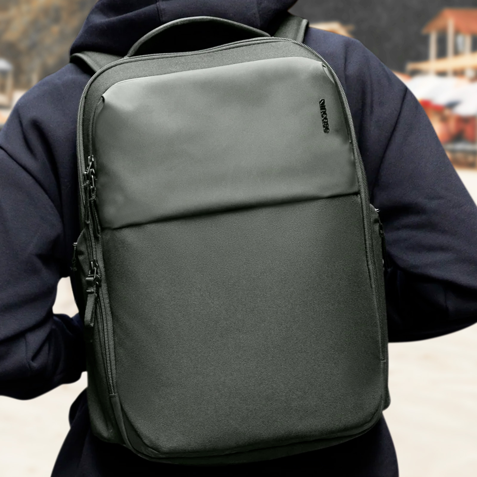 Ein Rucksack, der von einer Person getragen wird. Er ist dunkelgrau mit schwarzen Reißverschlüssen und einem schwarzen Incase-Logo.